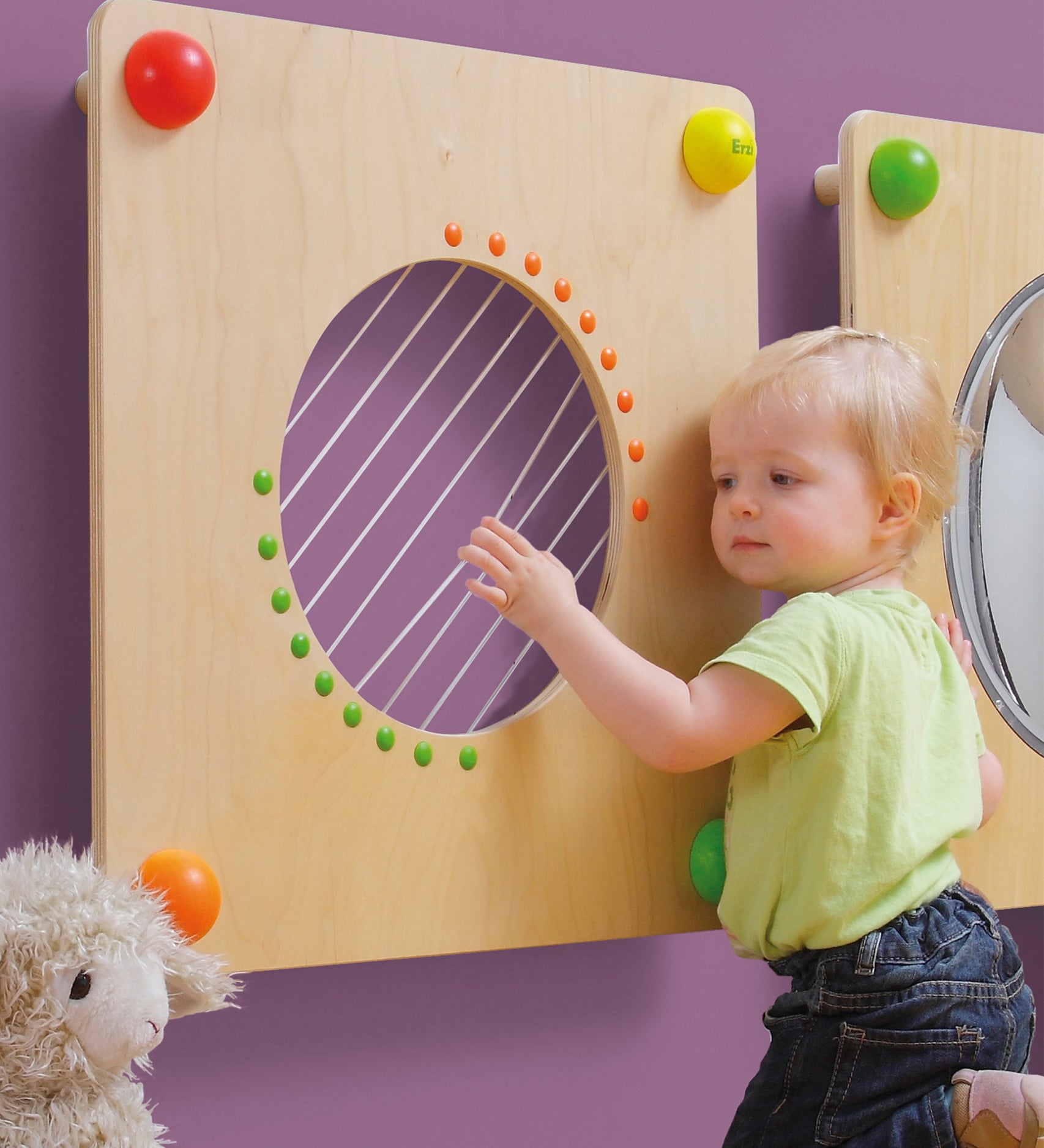 A child happily plucking the strings on the Erzi Baby Guitar Wall Board. Perfect for little musical maestros 