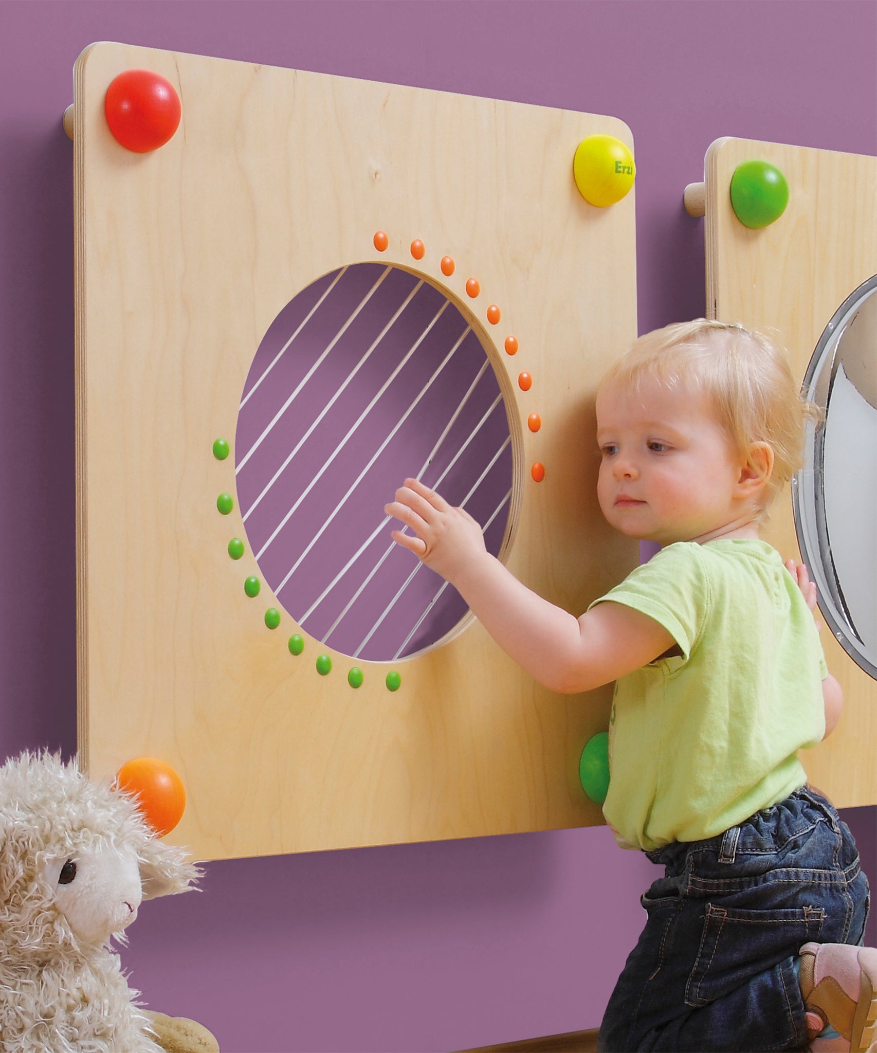 A child happily plucking the strings on the Erzi Baby Guitar Wall Board. Perfect for little musical maestros 