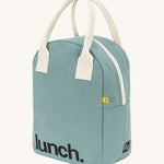 Fluf zip lunch bag in a light pastel blue colour with a white handle and lunch logo on the bottom with a white zip side detail on a cream background 