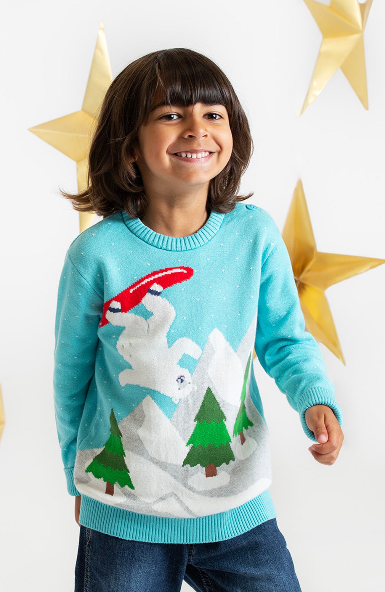 child wearing winter Frugi organic umper, smiling with gold stars hanging behind in background for a christmassy feel 