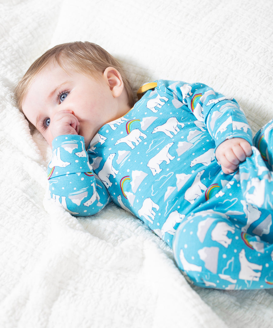 A baby lying on a white blanket, wearing the Frugi Easy Dressing Babygrow - Winter Tails