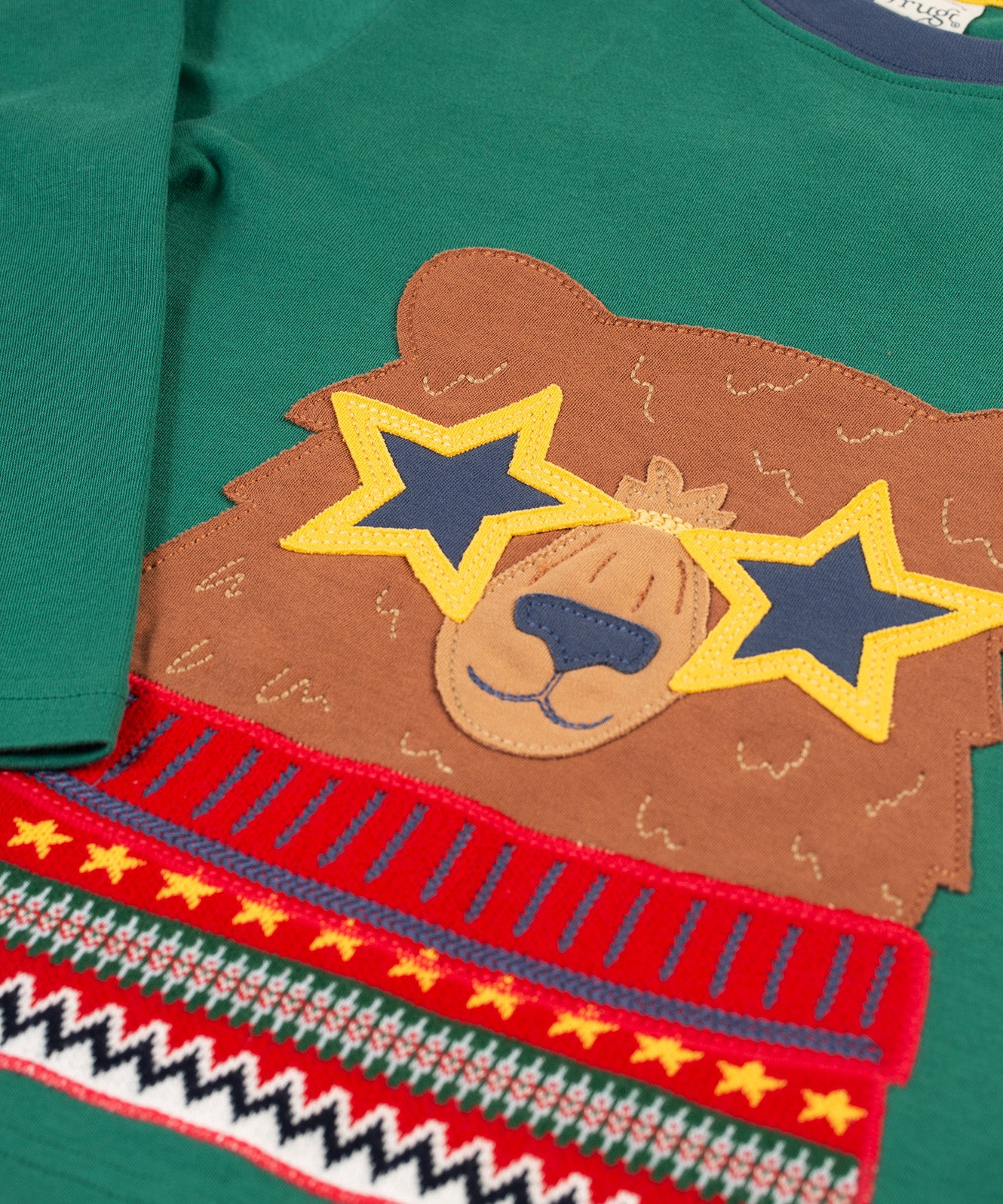 A closer look at the bear applique on the Frugi Terrific Applique Top - Teal/Fairisle Bear. The bear is light brown, with yellow star sunglasses, and wears a red patterned top, on teal green fabric