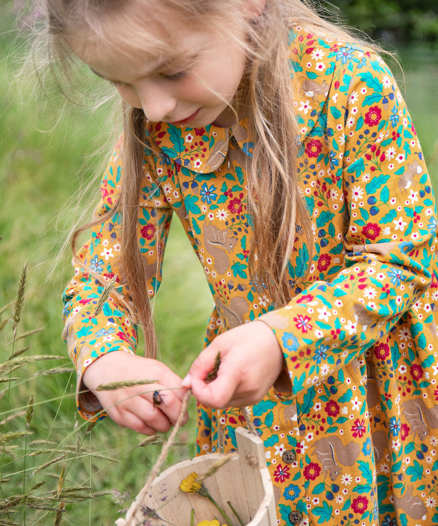 A child wearing the Frugi Autumn Dress - Autumn Friends, and playing with a beetle on their hand