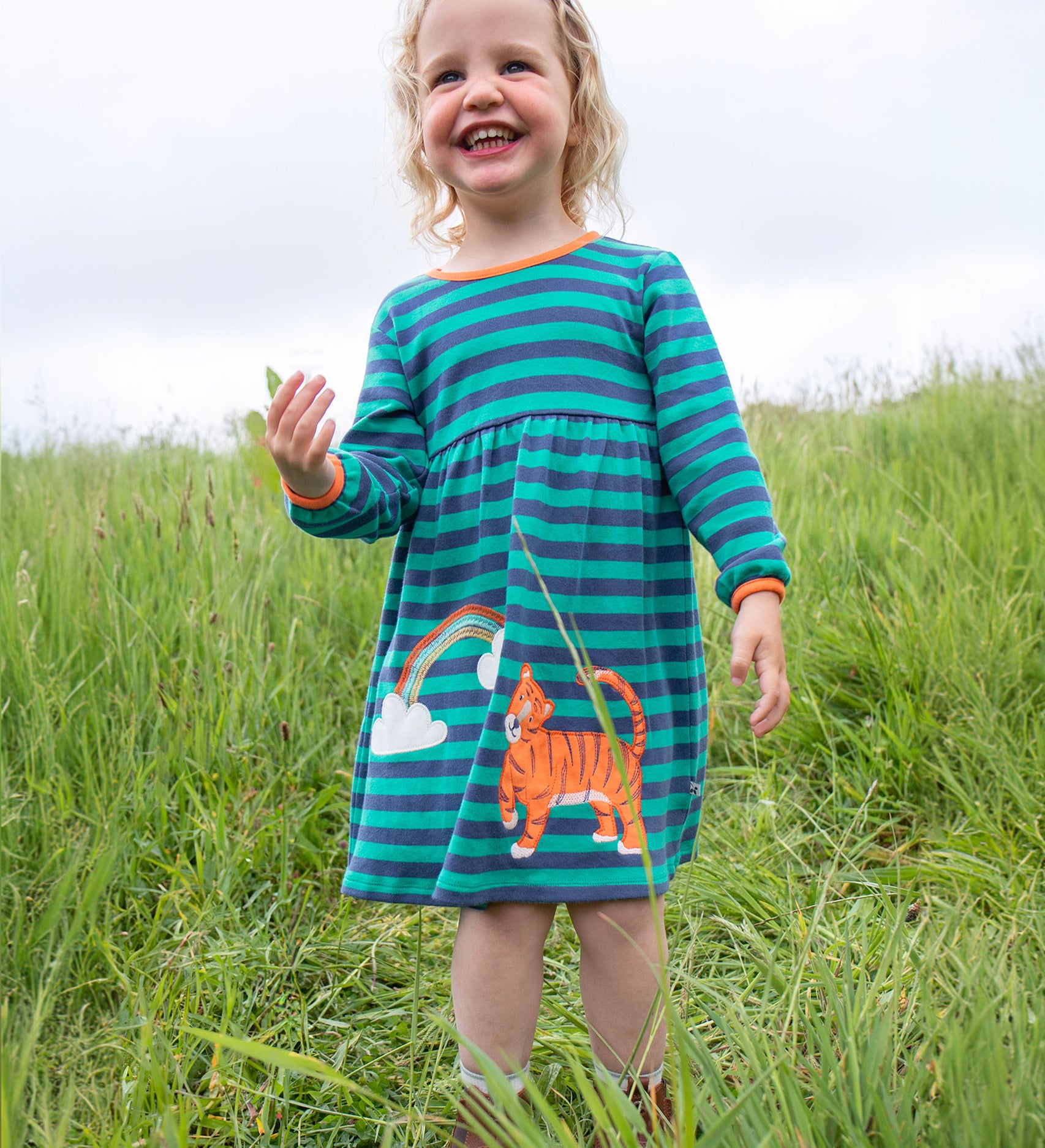 A child happily playing outside wearing the Frugi Dolcie Dress - Iguana Stripe/Tiger