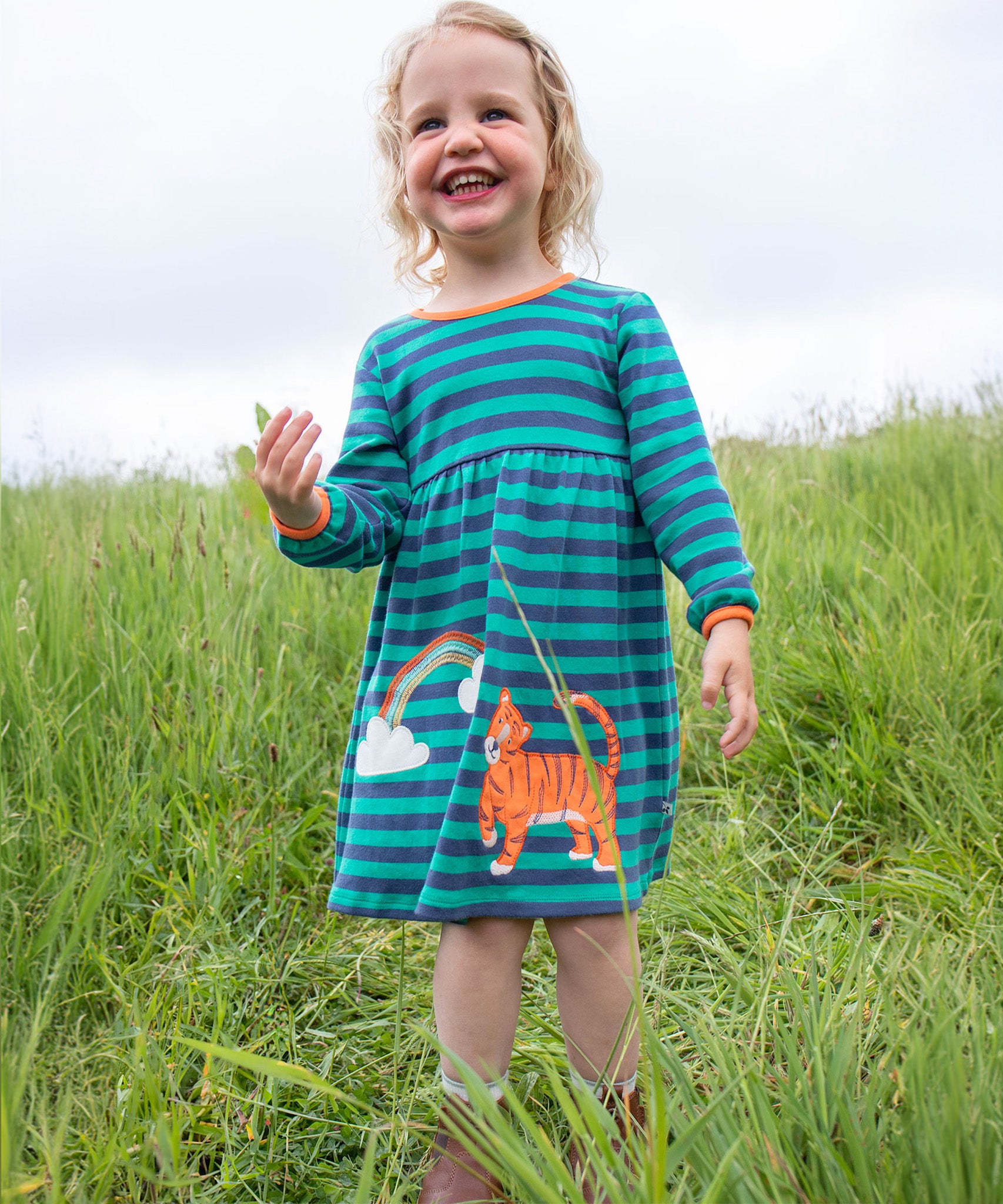 A child happily playing outside wearing the Frugi Dolcie Dress - Iguana Stripe/Tiger