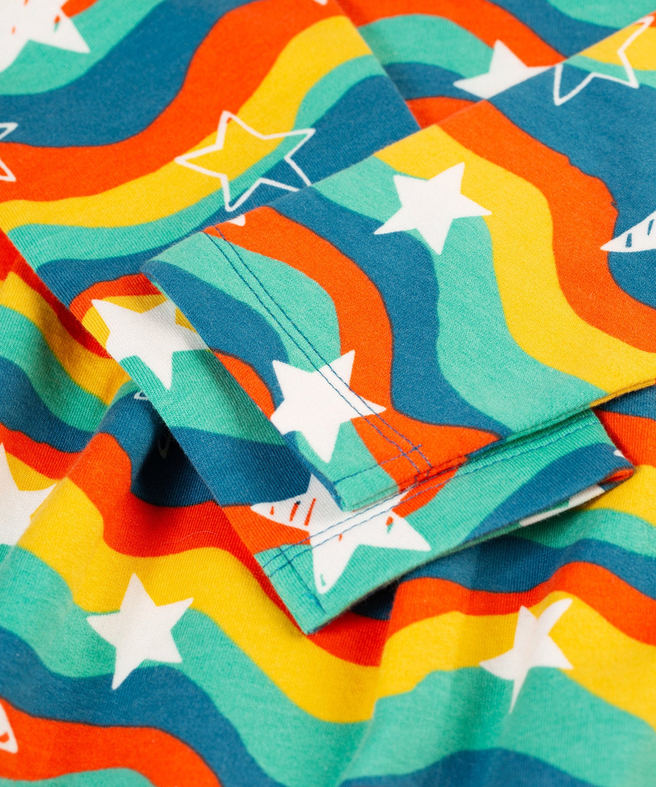 A closer look at the long sleeves, wavy rainbow stripe and white star print on the Frugi Cosy Amelia Dress - Wavy Stars