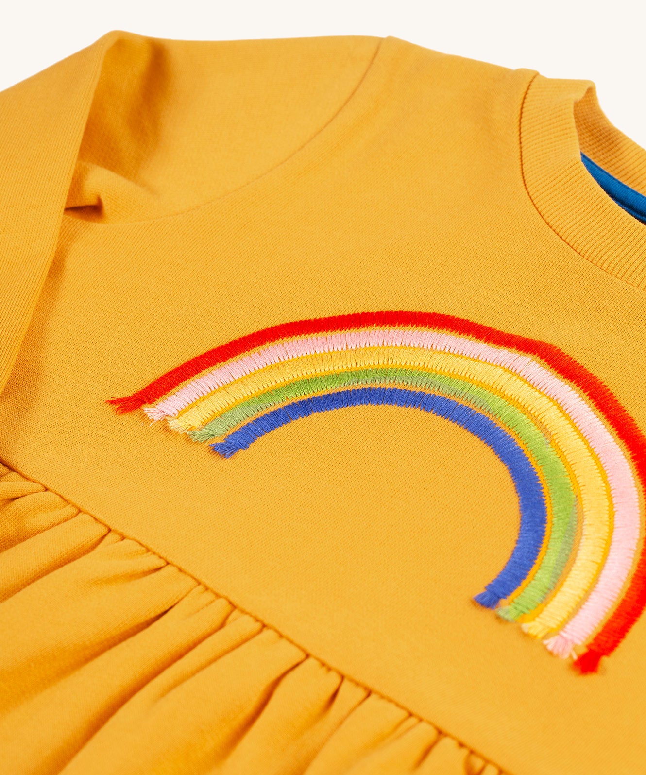 A closer look at the embroidered rainbow of ht from of the Frugi Niamh Dress - Gold/Rainbow. The colours are red, pink, yellow, green and blue