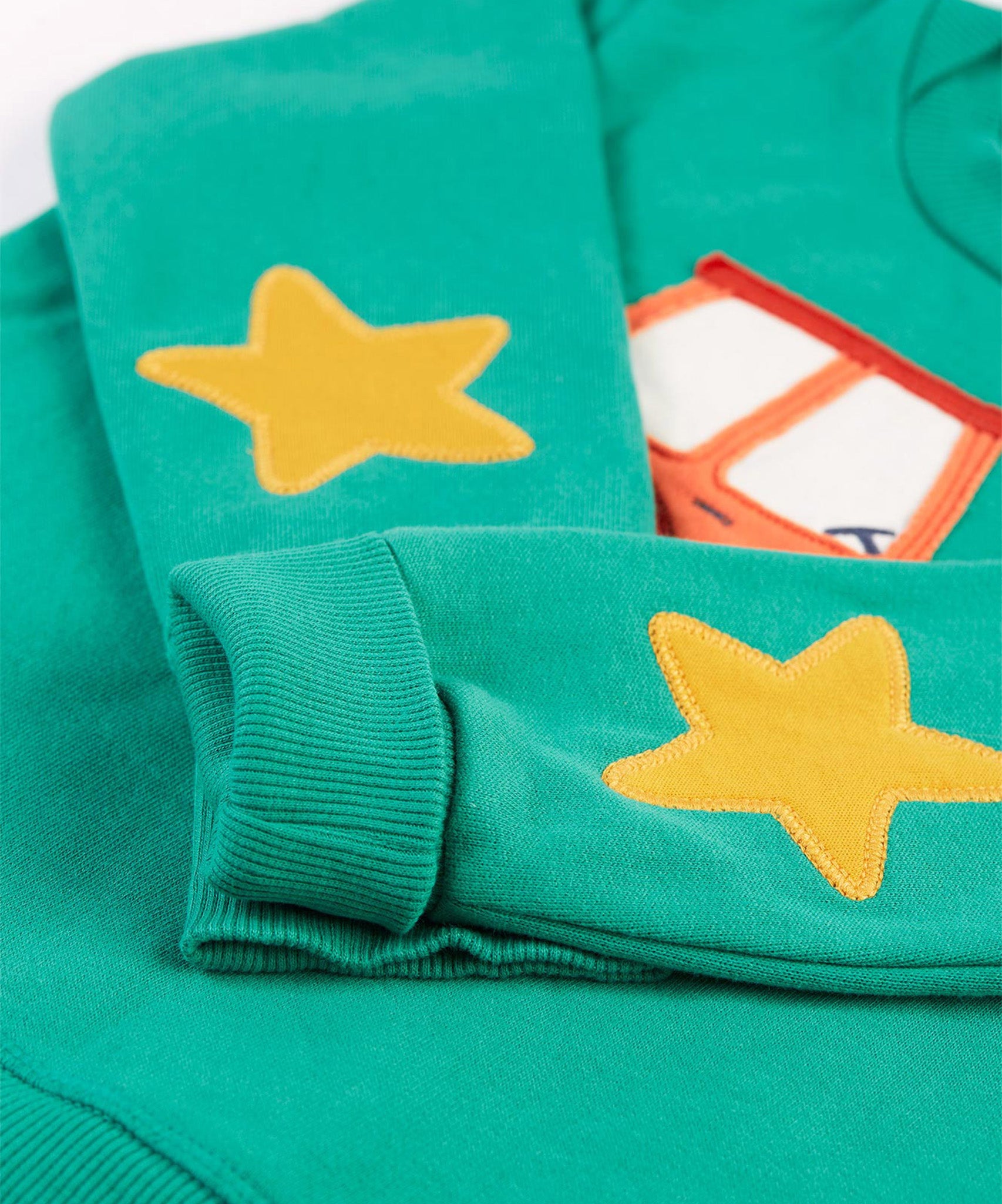 A closer look at the star applique patches on the sleeves of teh Frugi Easy On Jumper - Iguana/Tractor