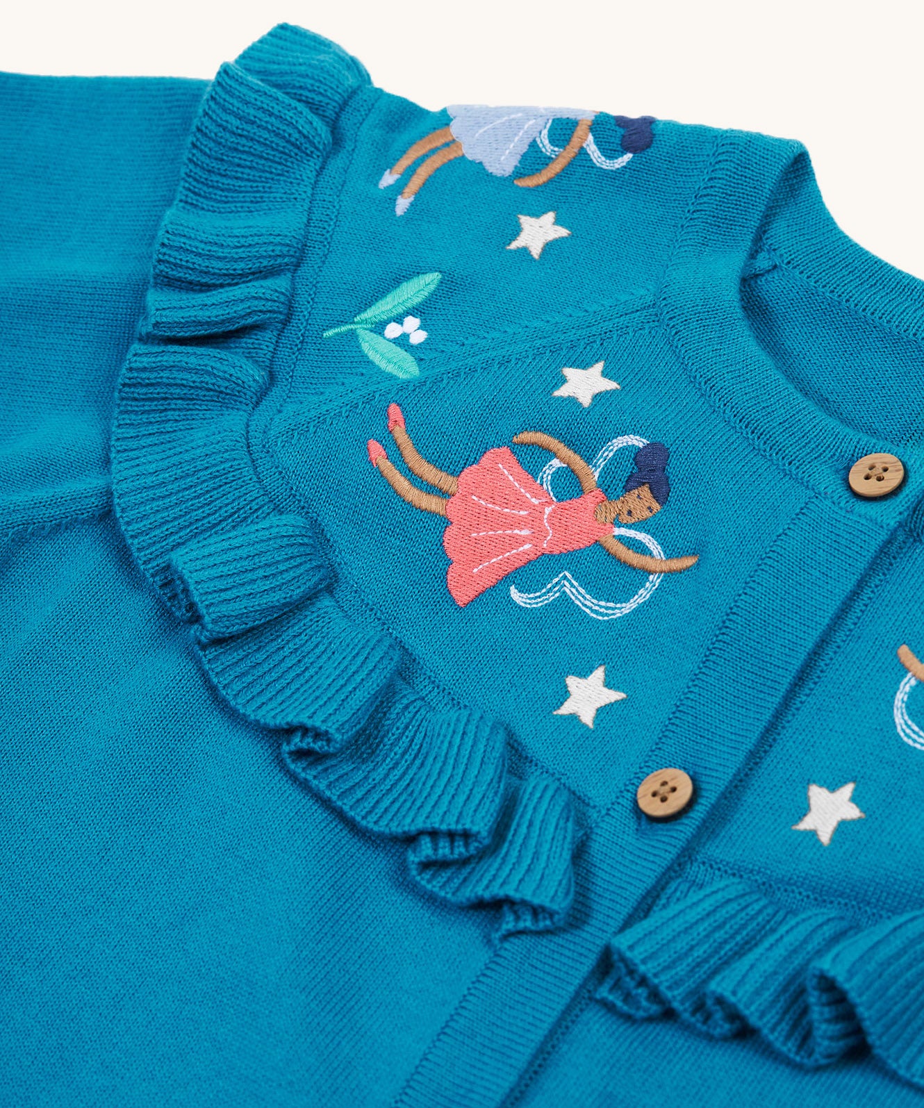 A closer look at the beautiful embroidered fairies on the Frugi Romi Ruffle Cardigan - Deep Water/Fairies. The image also shows the ruffled collar fabric, and stars surrounding the fairies.