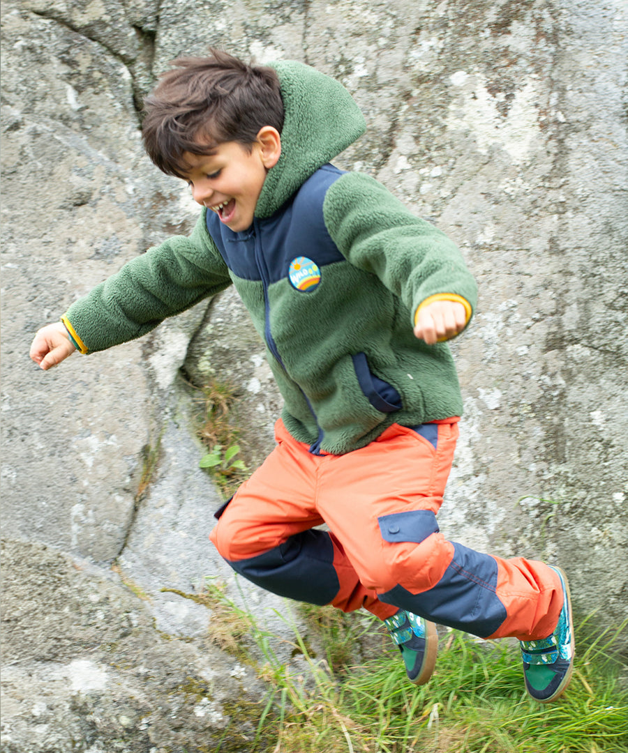 A child wears the Frugi Expedition Trousers - Paprika / Indigo in an outdoor setting.