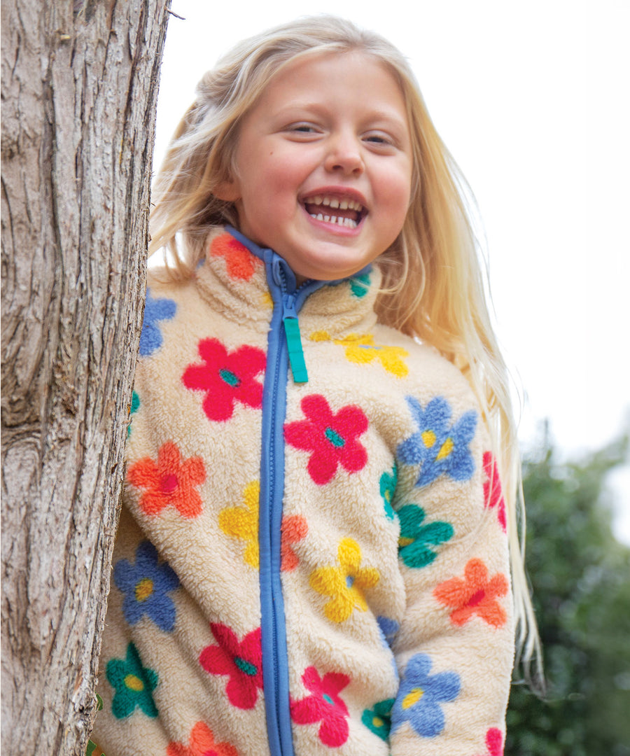 A child happily stood by a tree, wearing the Frugi Zipped Ted Fleece Jacket - Flower Pop