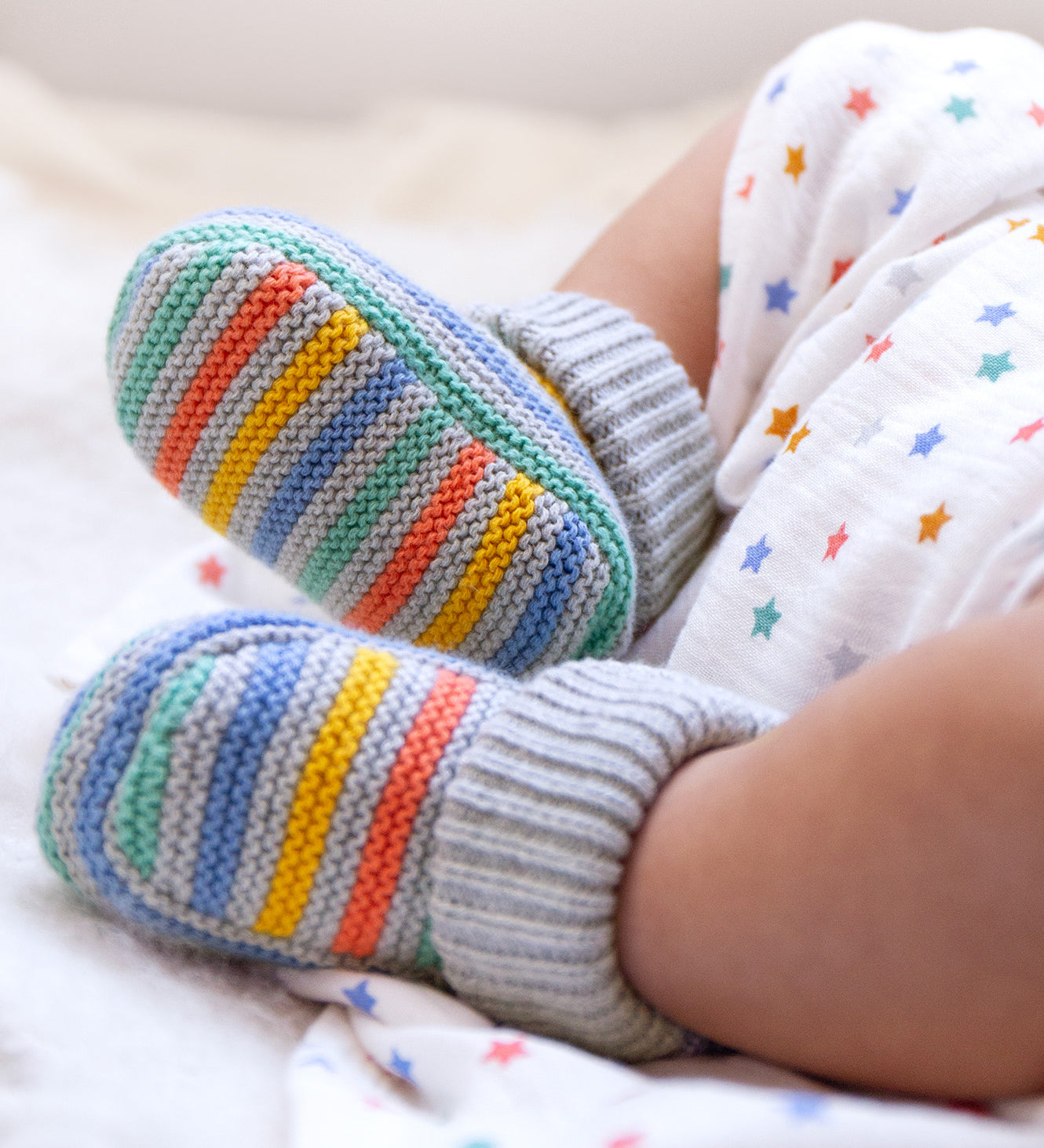 A closer look at the Frugi Briar Knitted Booties - Grey Marl Stripe, being worn by a baby