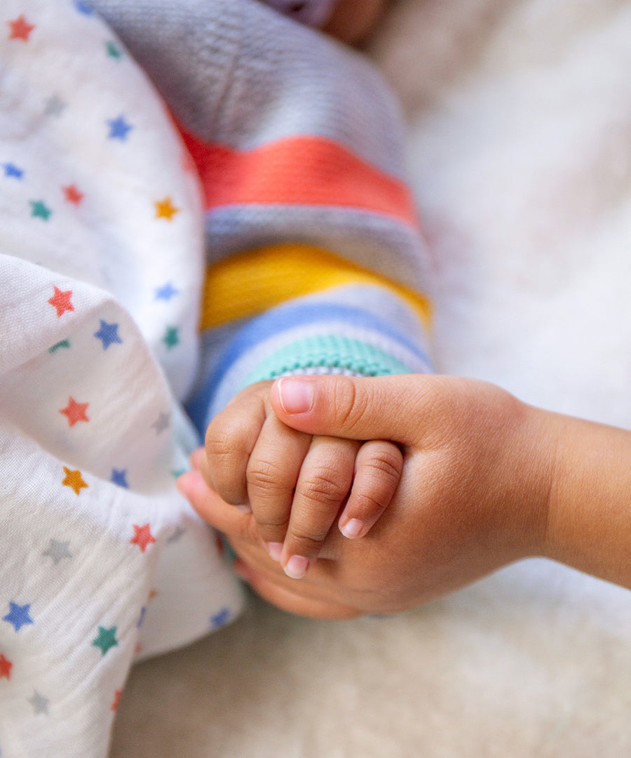 Two children's hands together, with the cardigan and stripes showing in the background