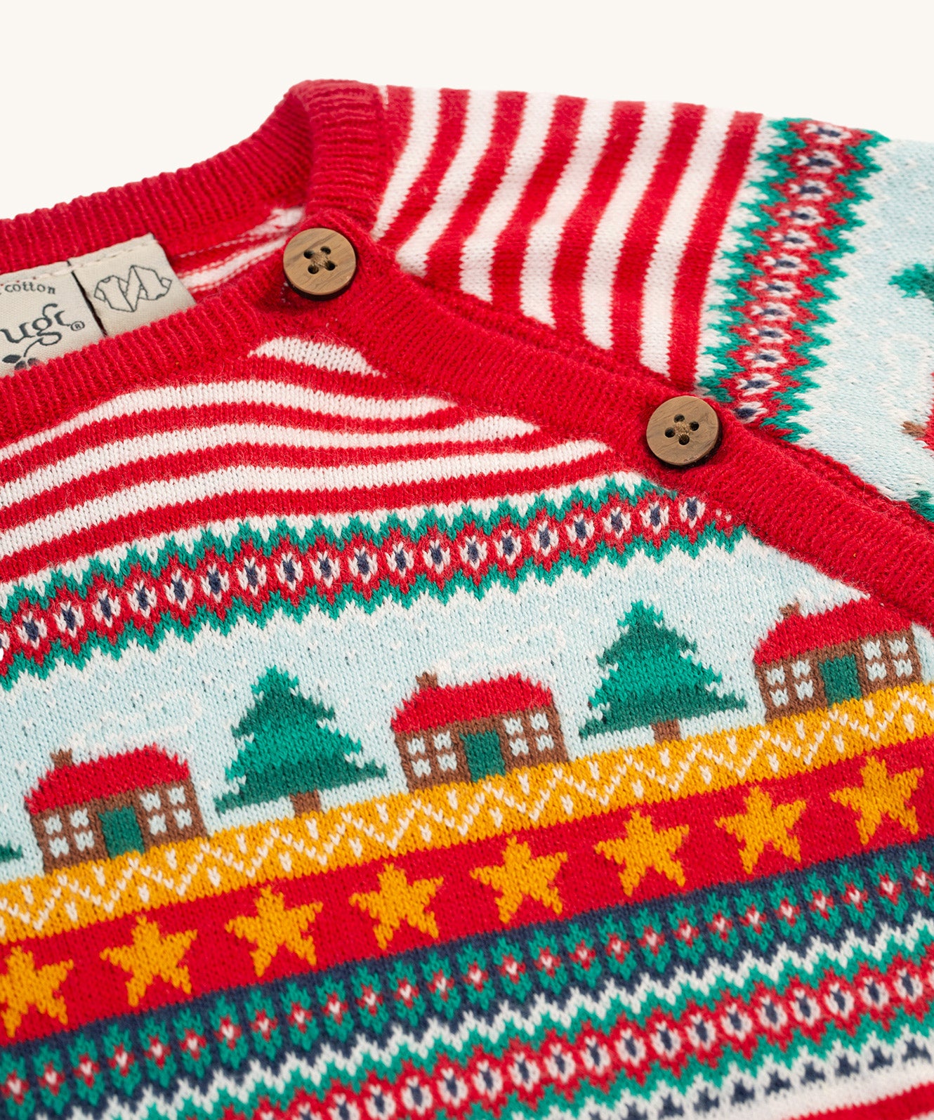 A closer look at the Christmas tree, house and star print on the Frugi Lumi Knitted Romper - Fairisle Christmas Stripe. Also shown are the buttons for easy on and off changing