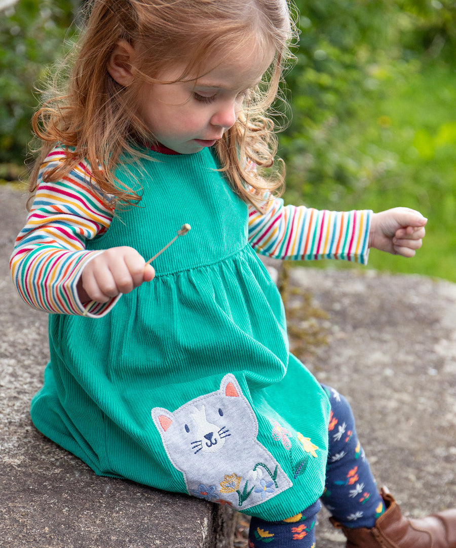 A child outside wearing the Frugi Betty Body - Lingonberry Multi-Stripe underneath a green Frugi cord dress and leggings