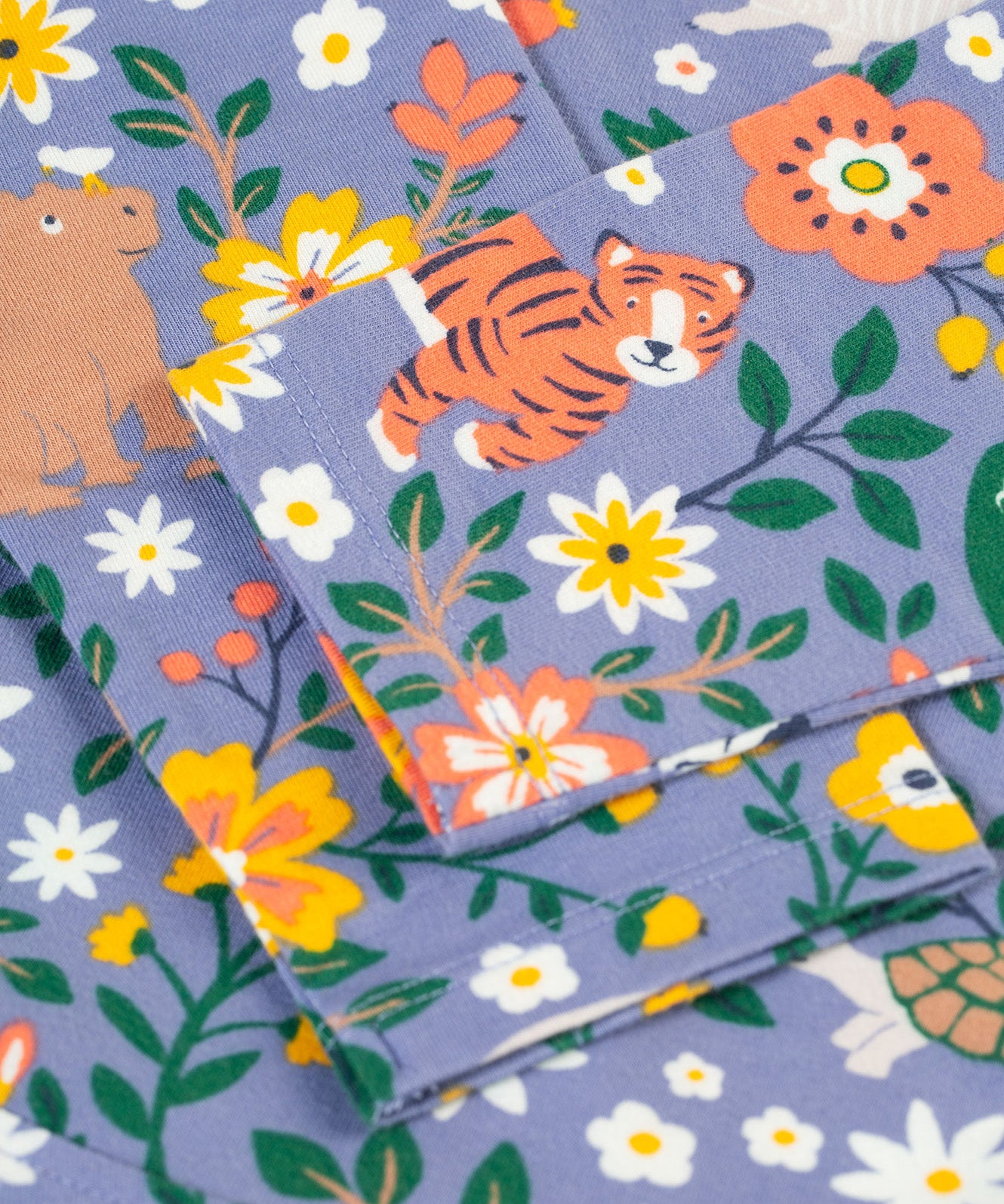 A closer look at the organic cotton Frugi Sofia Skater Dress - Rainforest Friends sleeves, and wildlife print. The image shows a happy tiger, rhino and flower/leaf prints