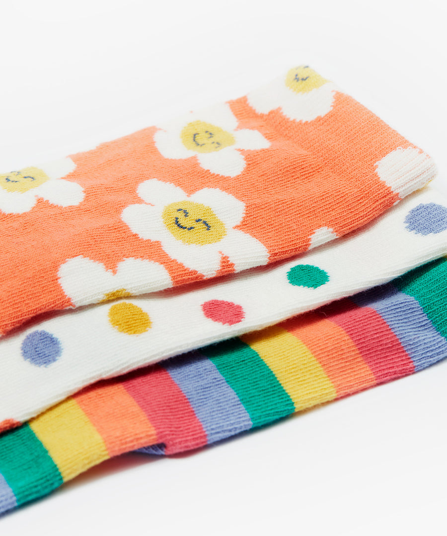 A closer look at the Frugi Rock My Socks - Stay Wild 3 Pack prints. The socks are laid on top of each other with the top sock being the orange and flower print, the middle sock is the white and polka dot print, and the bottom sock is the rainbow stripe print