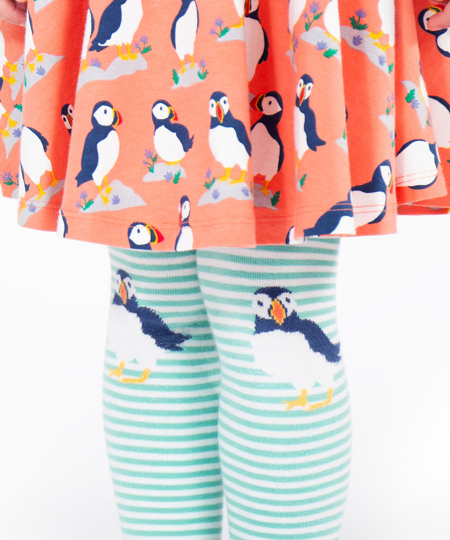 A closer look at the puffin print on the knees of the Frugi Norah Tights - Moss/Puffin, worn with a Frugi puffin dress