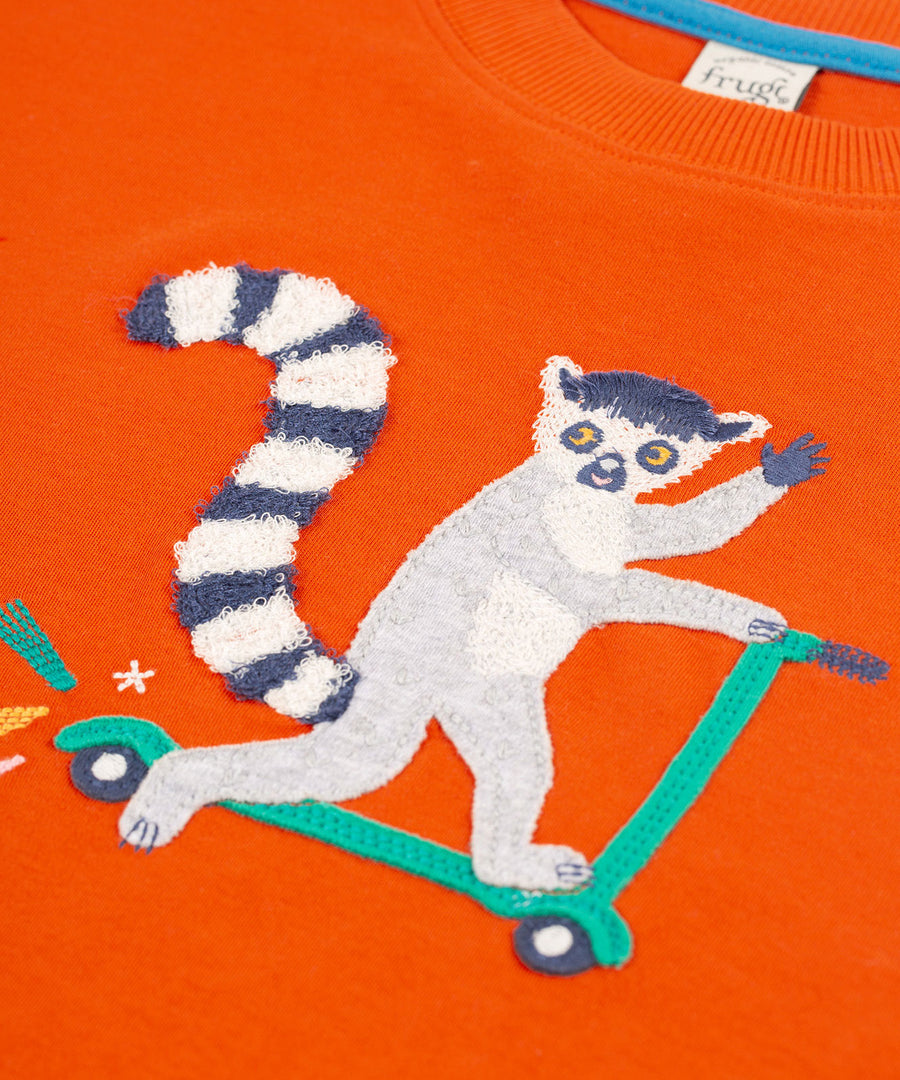 A look and the fun lemur, riding a scooter on the front of the Frugi Owen Top - Bonfire/Lemur