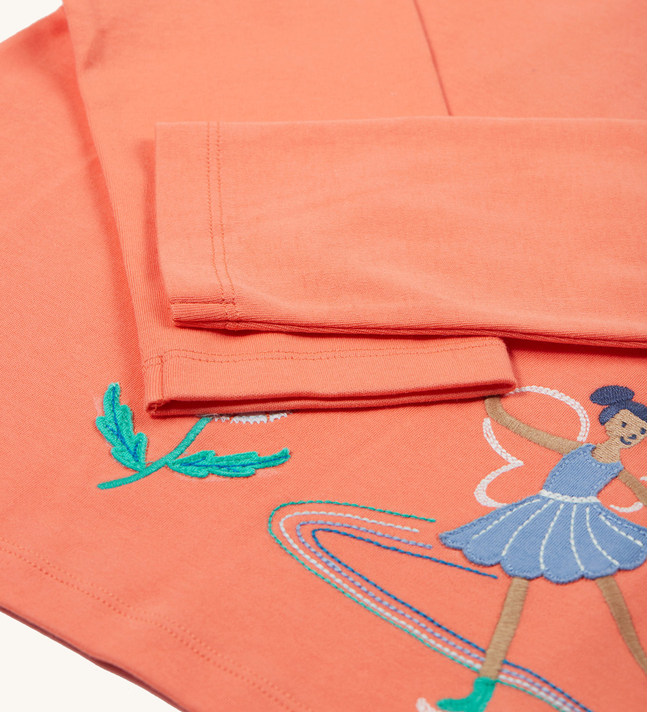 The long sleeves on the Frugi Anna Applique Top - Cantaloupe/Fairy. The fairy applique is partially shown on the bottom right corner