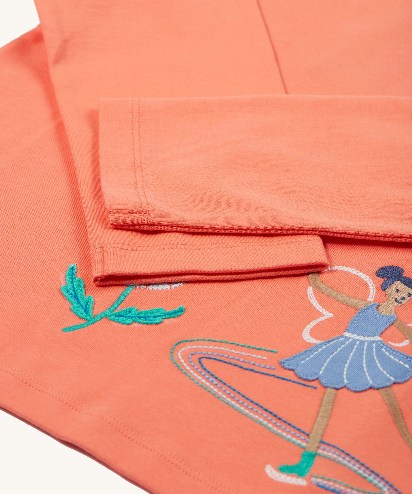 The long sleeves on the Frugi Anna Applique Top - Cantaloupe/Fairy. The fairy applique is partially shown on the bottom right corner