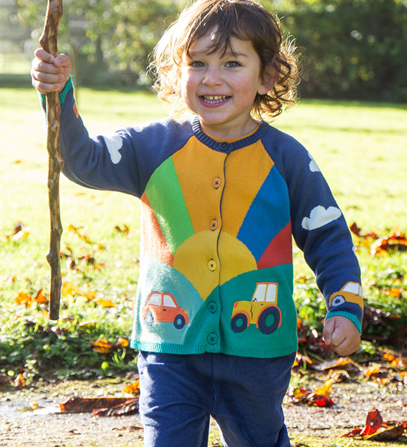 A child playing outside, wearing the Frugi Reva Applique Cardigan - Navy Blue/Sunrise