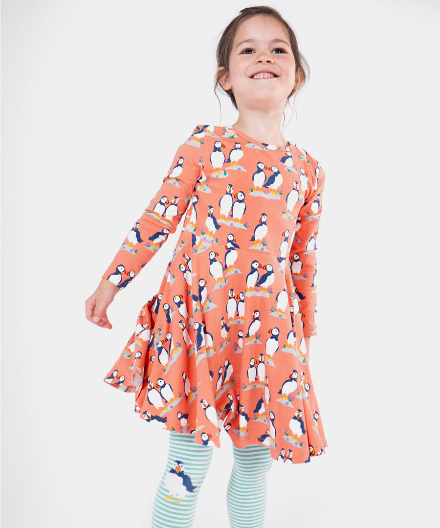 A child wearing the Frugi Sofia Skater Dress - Puffin Pals, with Frugi puffin stripe tights