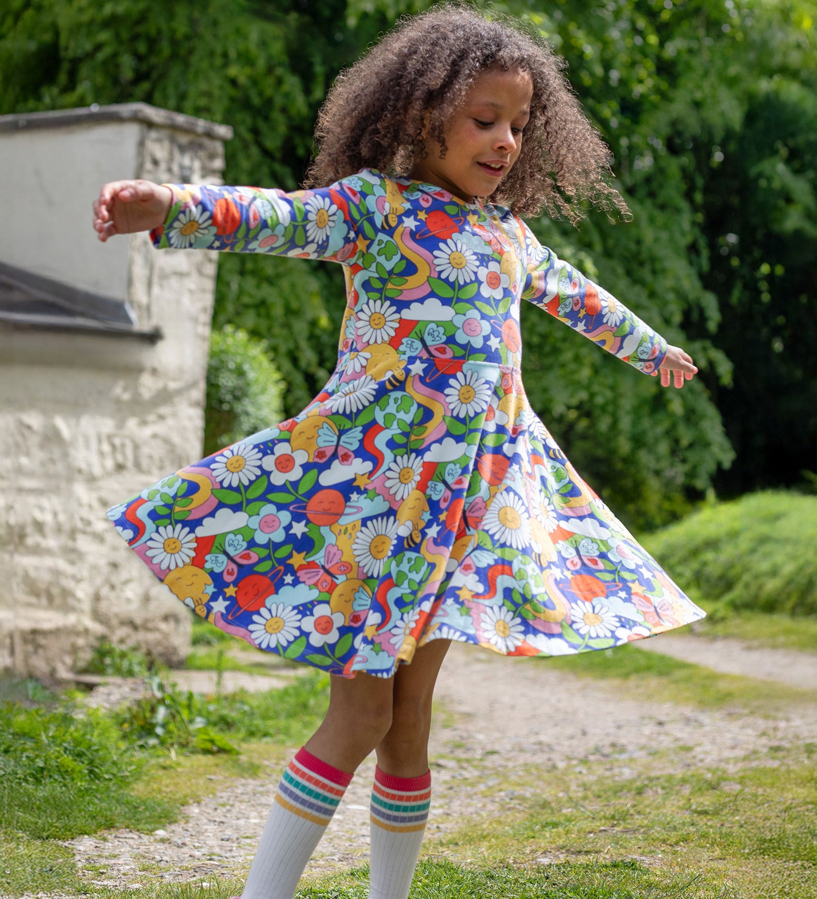 A child playing outside, twirling in the Frugi Sofia Skater Dress - Retro Happy, to show the movement and flow of the dress skirt.