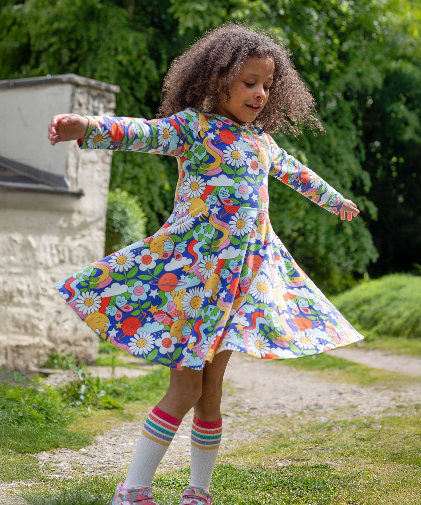 A child playing outside, twirling in the Frugi Sofia Skater Dress - Retro Happy, to show the movement and flow of the dress skirt.