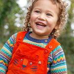 A child happily playing outside whilst wearing the Frugi Durgan Cord Dungaree - Bonfire/Tiger