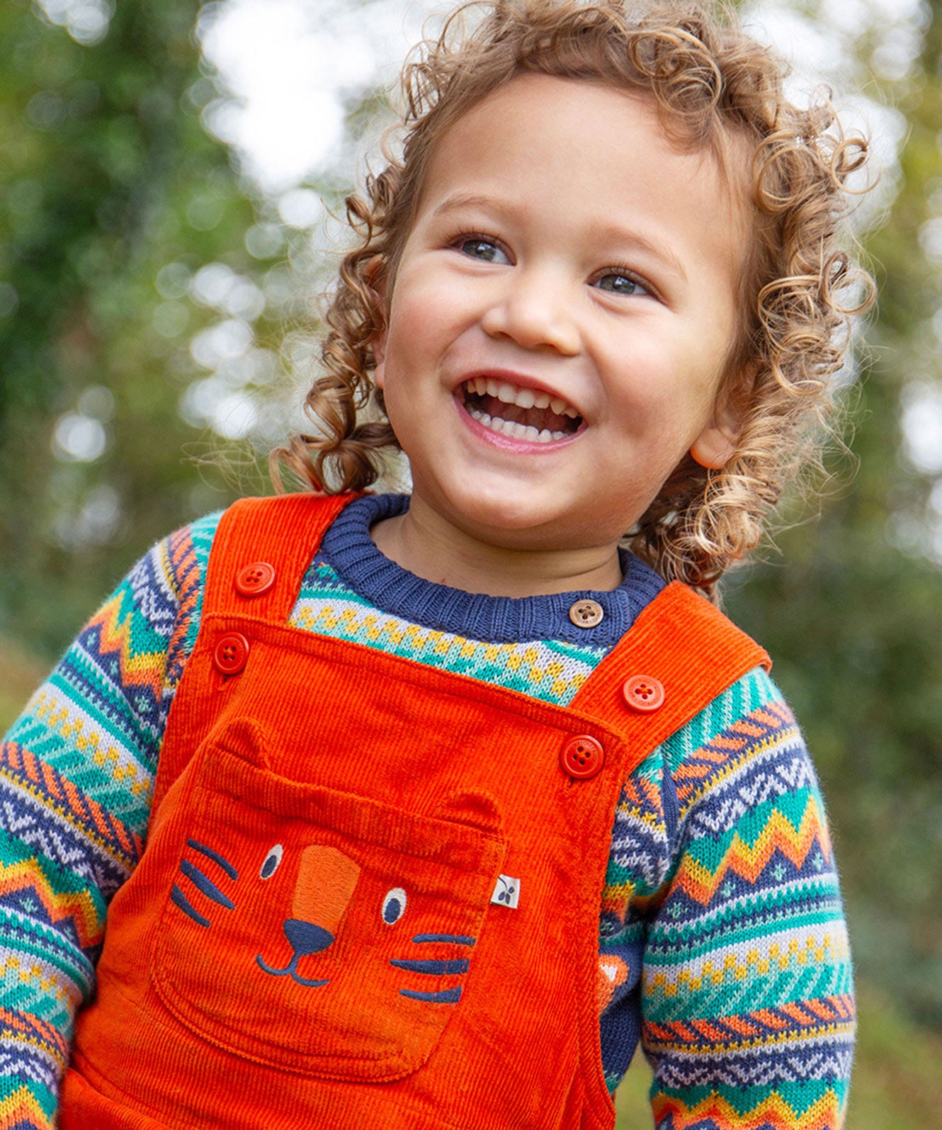 A child happily playing outside whilst wearing the Frugi Durgan Cord Dungaree - Bonfire/Tiger