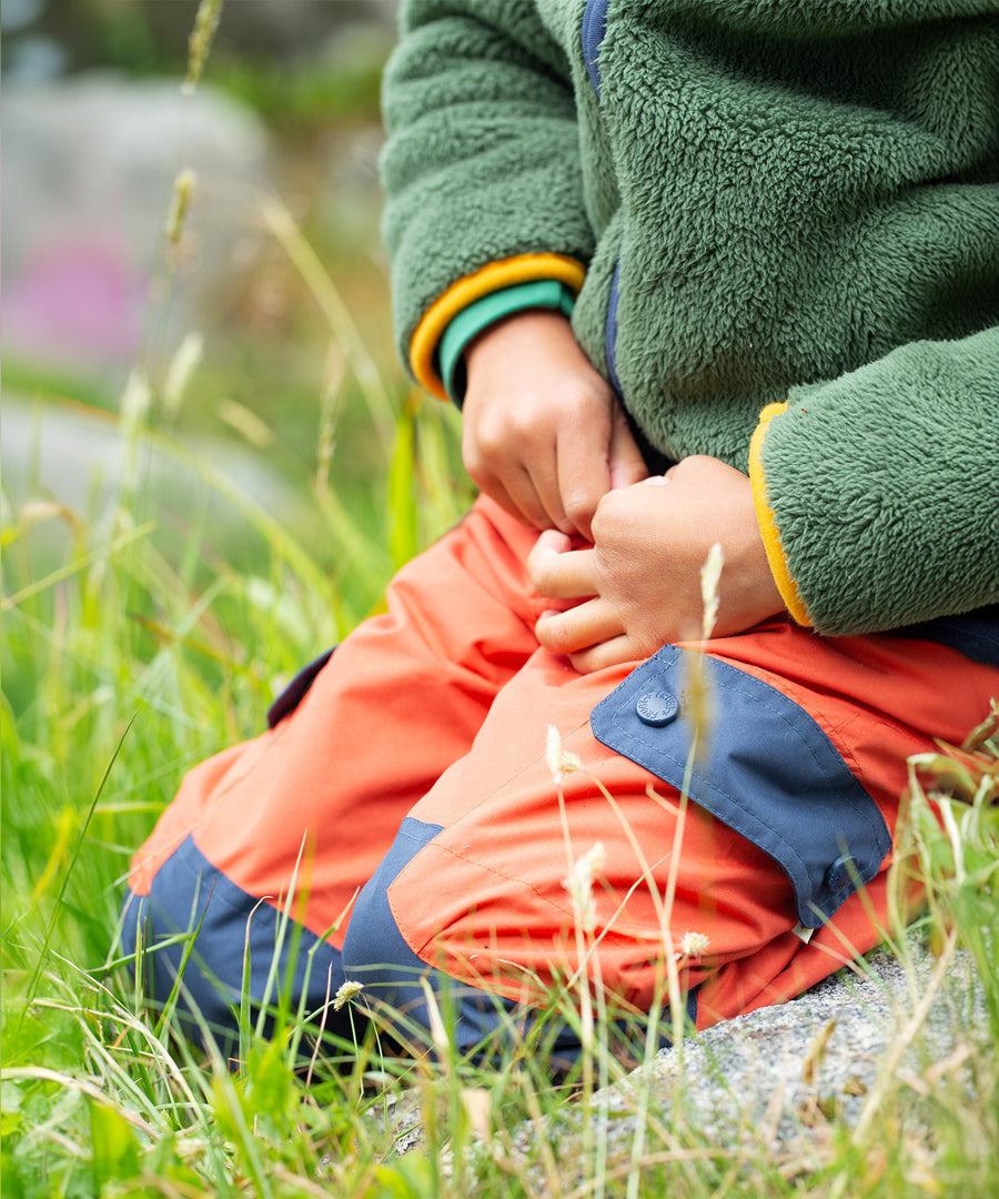 Material and pocket detail on the Frugi Expedition Trousers - Paprika / Indigo in an outdoor setting.