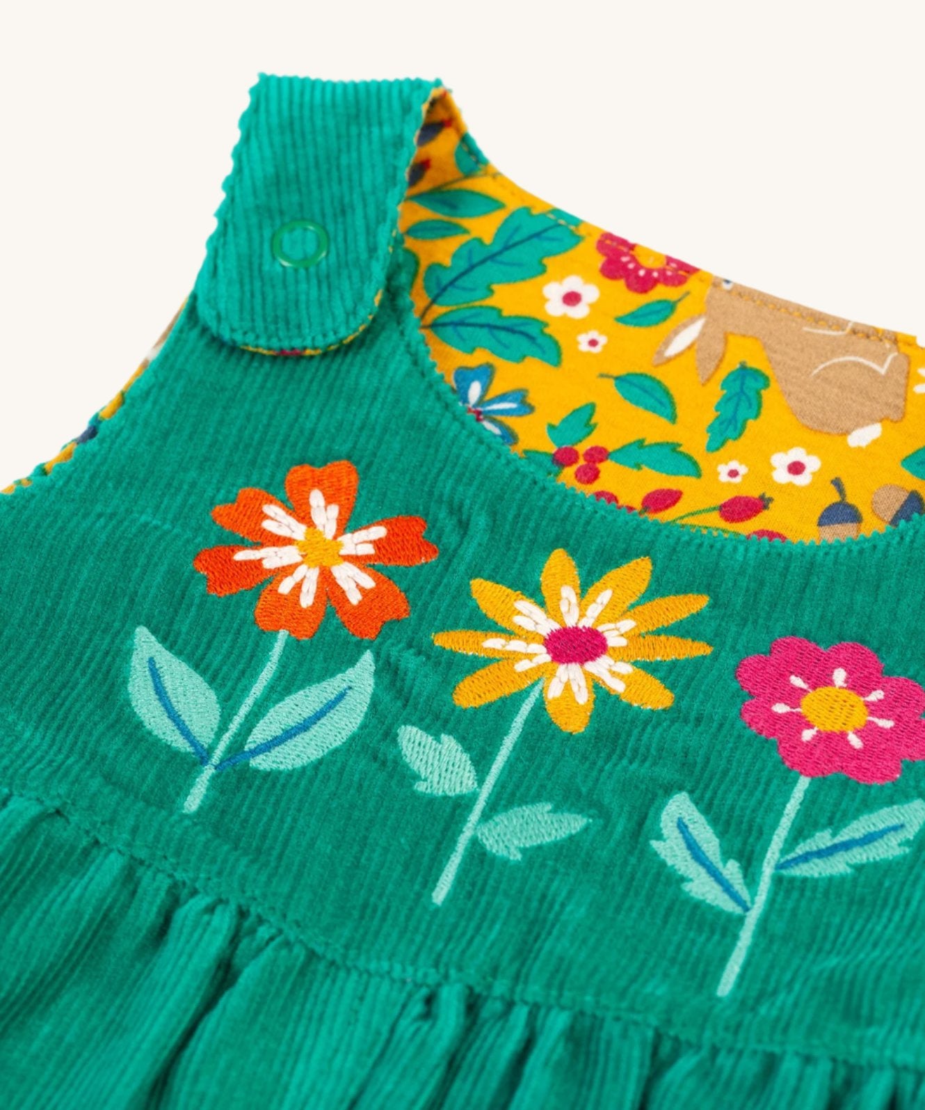 A closer look at the green cord side of the Frugi Lacey Reversible Dungaree - Iguana/Autumn Friends. Showing the popper shoulder straps, and flower applique details on the front