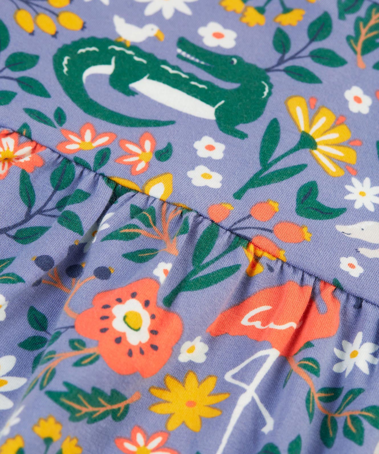 A closer look at the dress skirt gathering on the Frugi Dee Dress - Rainforest Friends, and dress print. The dress is a lilac colour, and in this image the print shows a crocodile, a flamingo, an anteater, beautiful flowers and leaves in different colours.