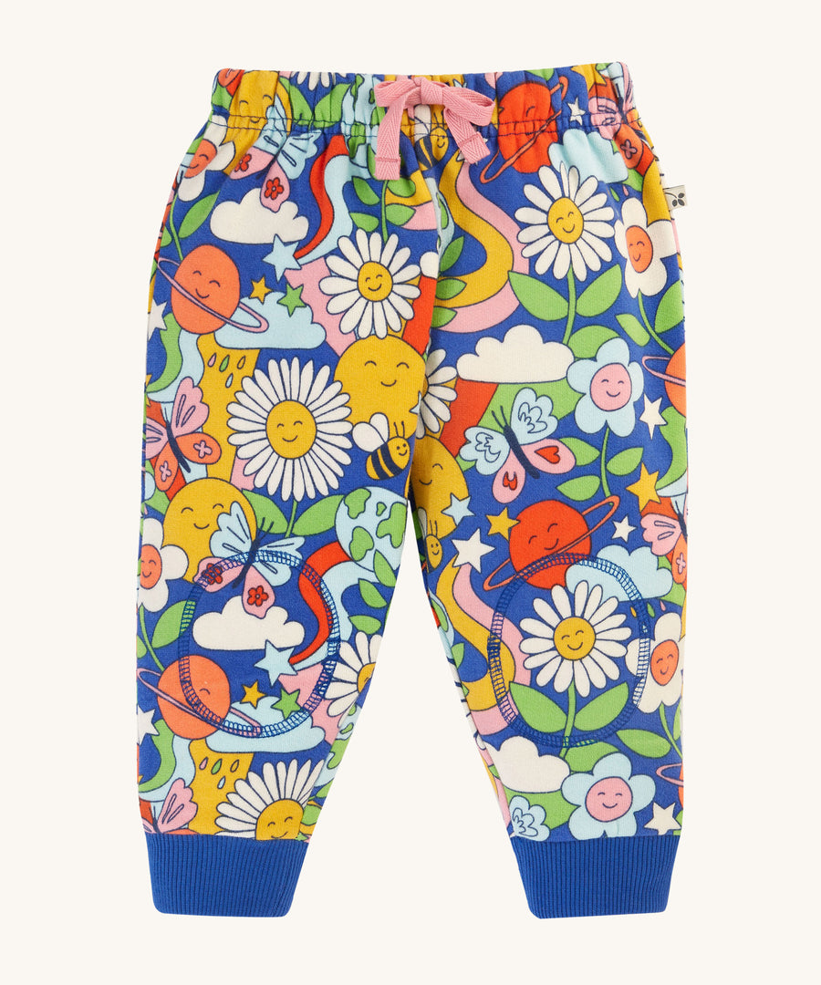 Frugi Snuggle Crawlers - Retro Happy. A fun retro print pair of trousers with a soft, double layer on the knees to protect crawling children. They also have stretchy rib ankle cuffs, an elasticated waistband, and an adjustable drawcord on the waist. The pattern on these trousers is smiling planets, flowers, stars, bees, butterflies, clouds and rainbows