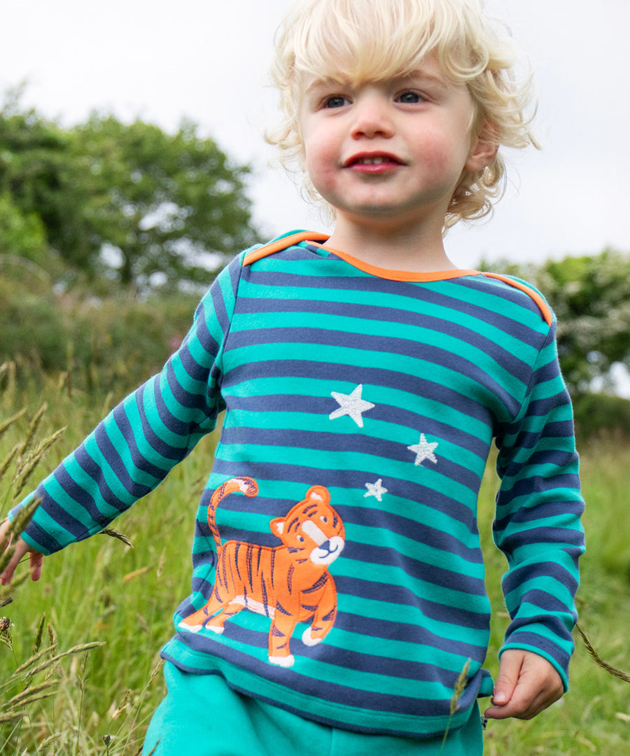 A child playing outside, wearing the Frugi Bobby Applique Top - Iguana Stripe/Tiger