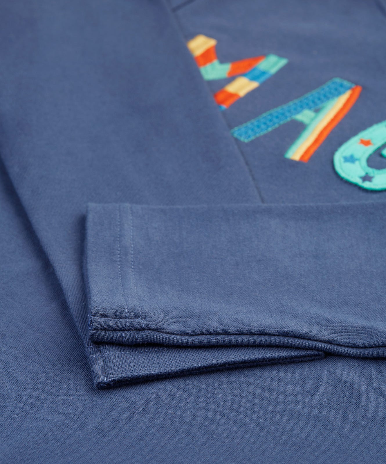 The navy sleeves on the Frugi Adventure Applique Top - Navy Blue/Magic, with some of the applique and embroidered letting showing partially under the folded sleeves