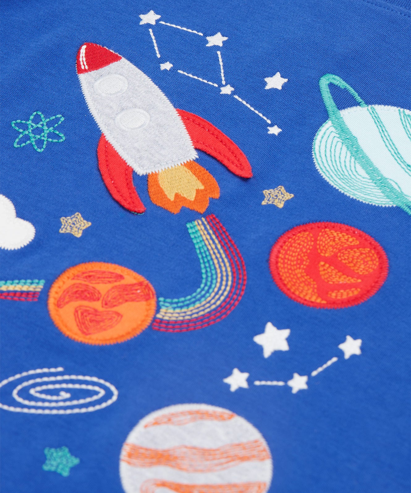 A closer look at the rocket and planet applique details on the Frugi Little Creature Applique Top - Blue Tang/Rocket. which includes embroidered space details