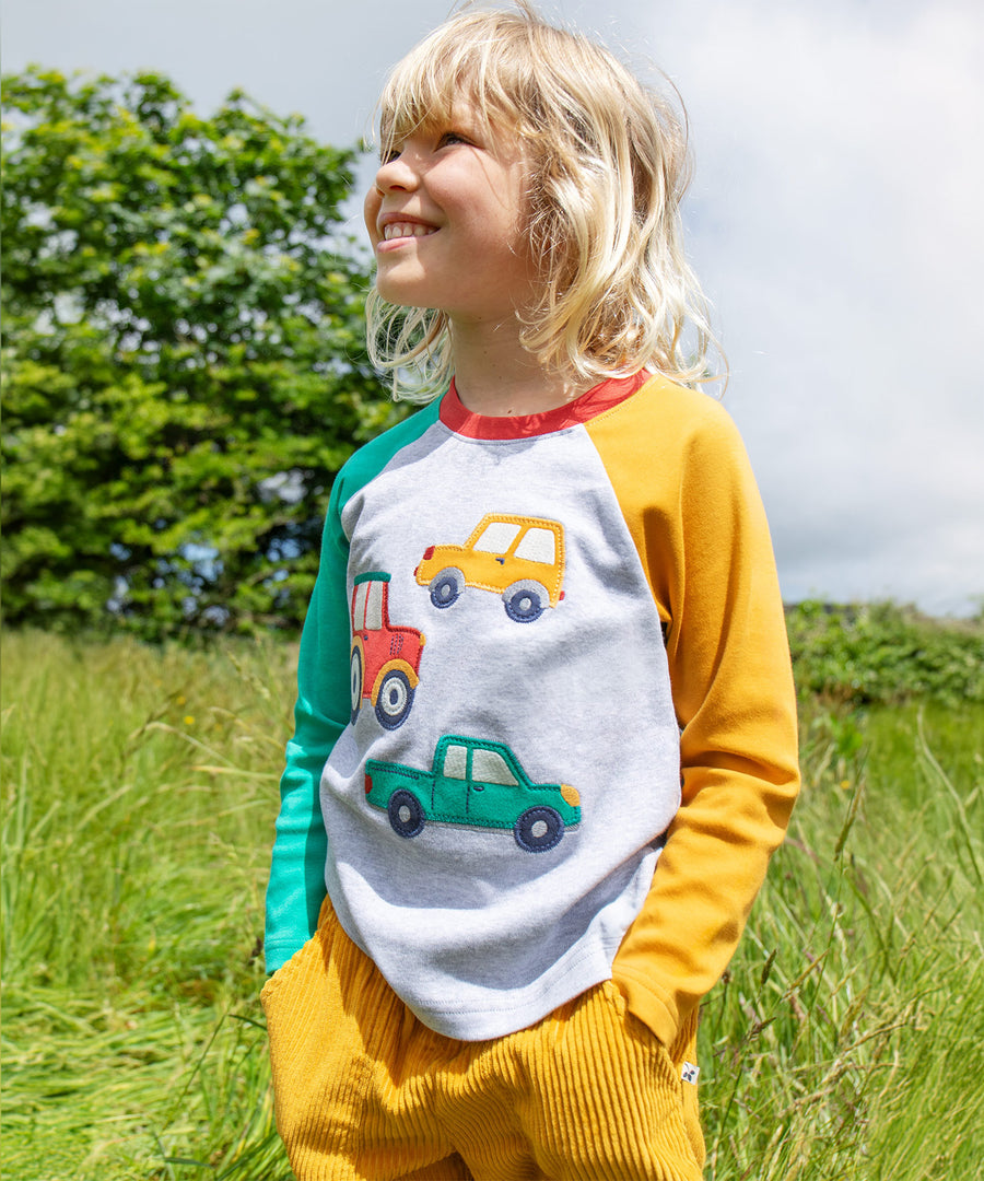 A child wearing the Frugi Alfie Raglan Top - Grey Marl/Vehicles outside in the sun