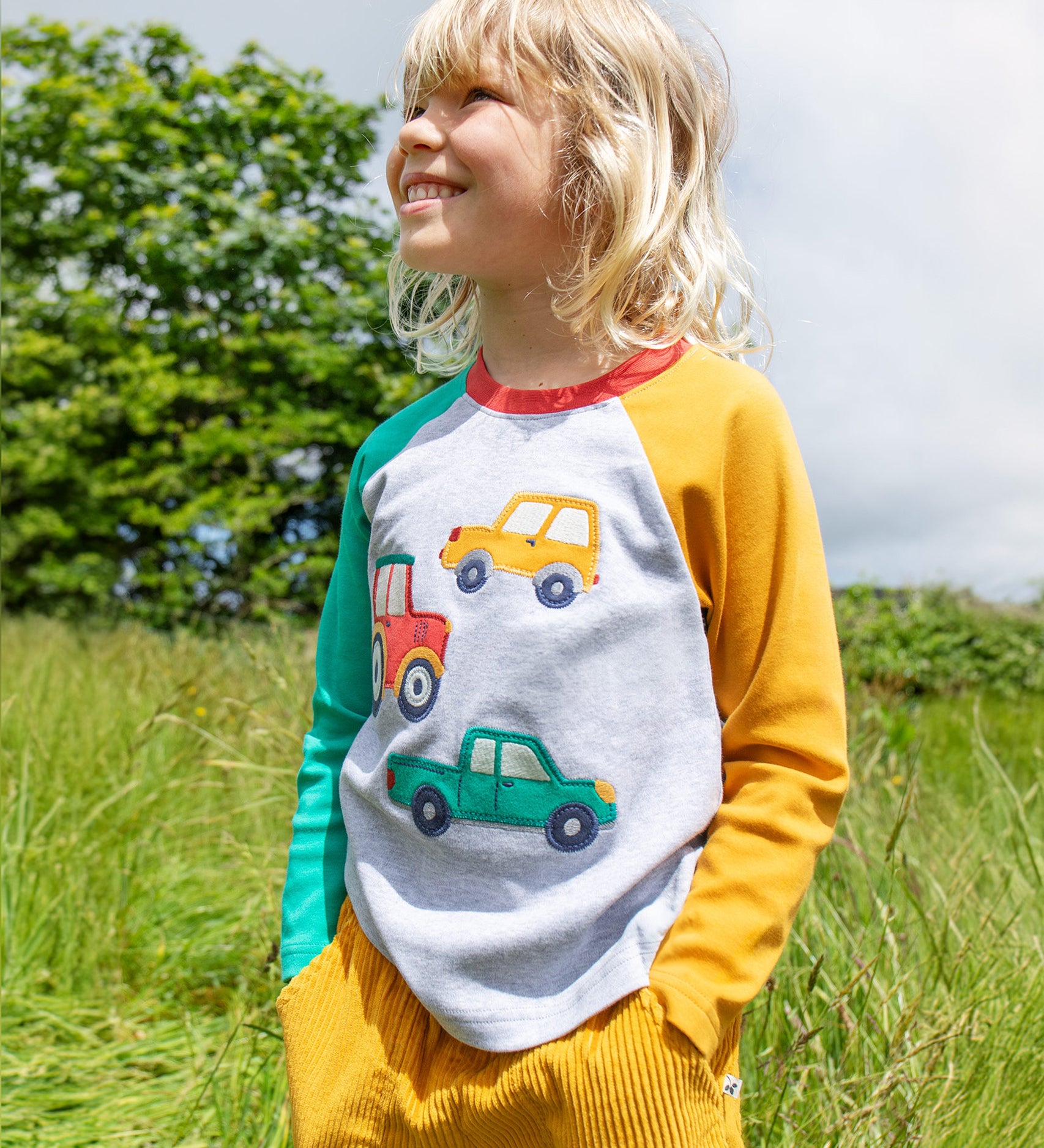 A child wearing the Frugi Alfie Raglan Top - Grey Marl/Vehicles outside in the sun