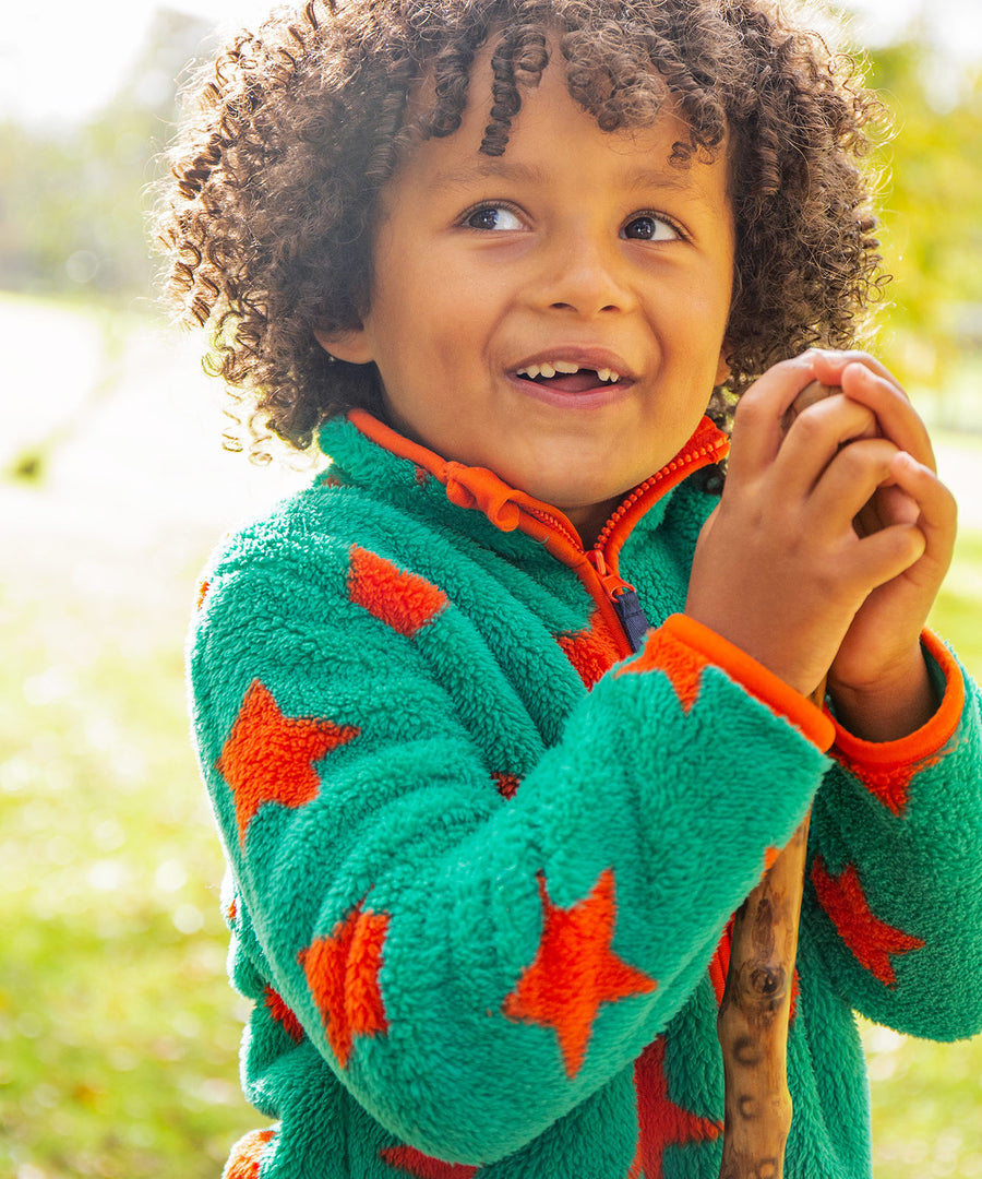 A child outside in the sun, wearing the Frugi Zipped Ted Fleece Jacket - Bonfire Stars