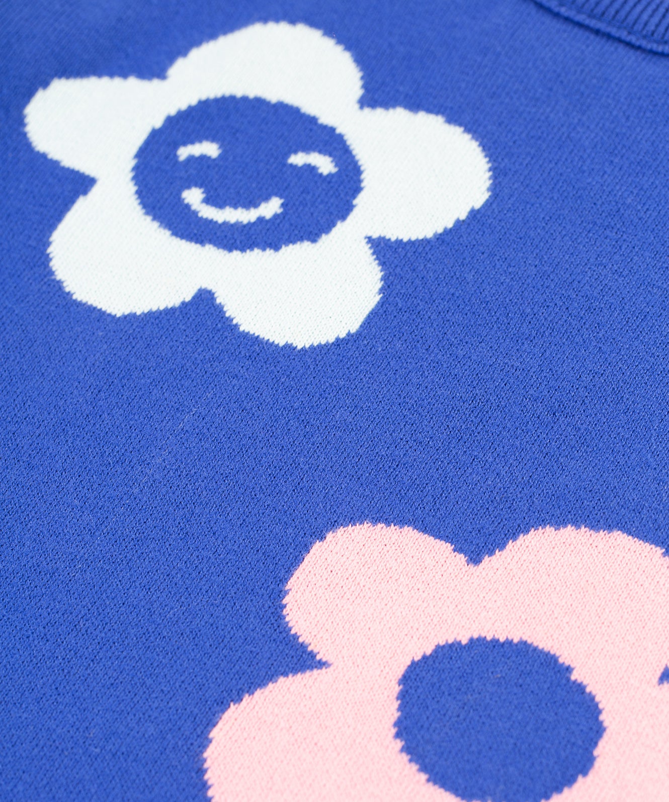 A closer look at the blue fabric and floral prints on the Frugi Zola Reversible Knitted Dress - Blue Tang/Retro Floral. The dress fabric looks very soft, and the flowers are white with a smily face, and a light baby pink