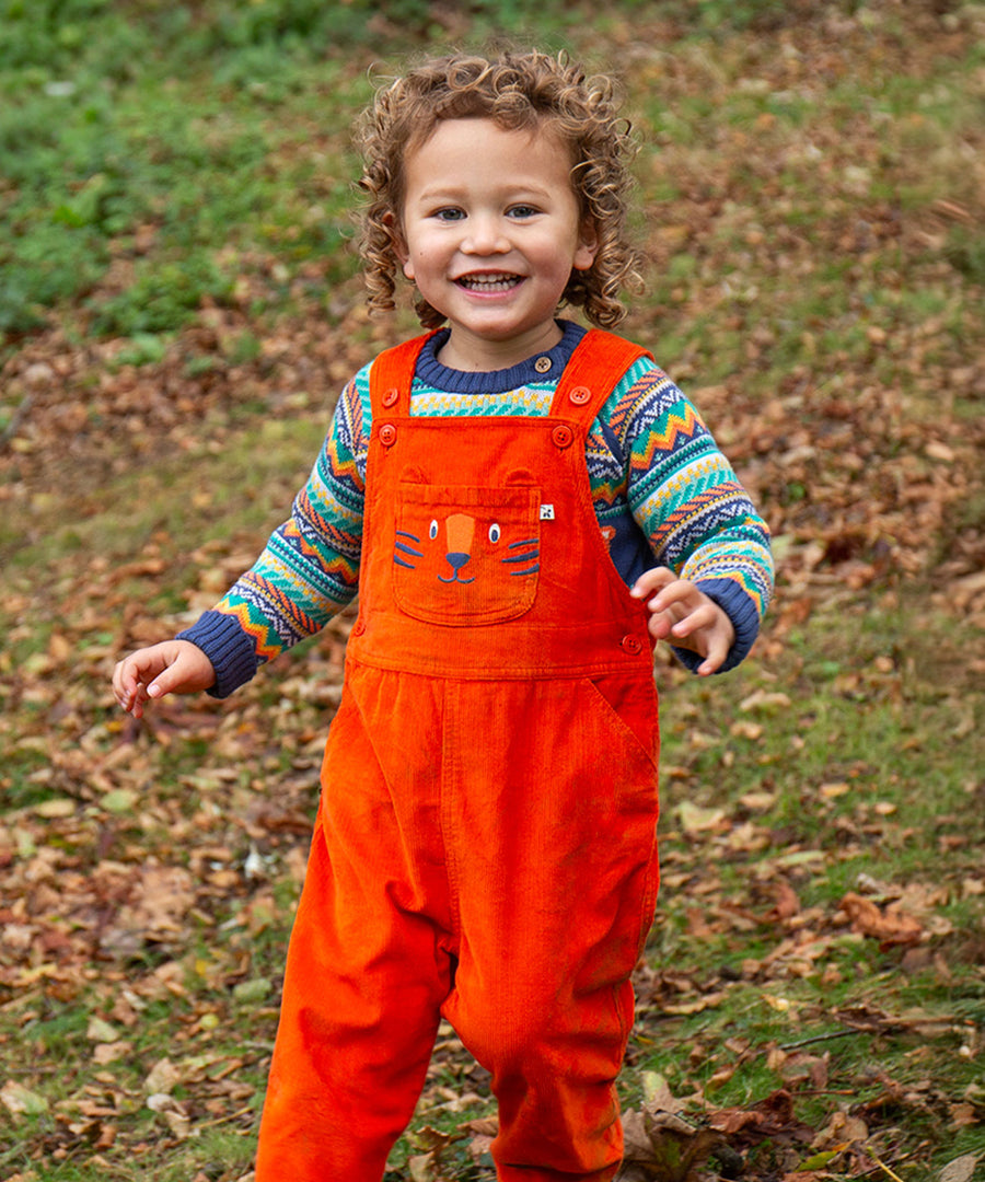 A child happily pleaying outside whilst wearing the Frugi Durgan Cord Dungaree - Bonfire/Tiger and a colourful Frugi jumper