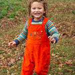 A child happily pleaying outside whilst wearing the Frugi Durgan Cord Dungaree - Bonfire/Tiger and a colourful Frugi jumper