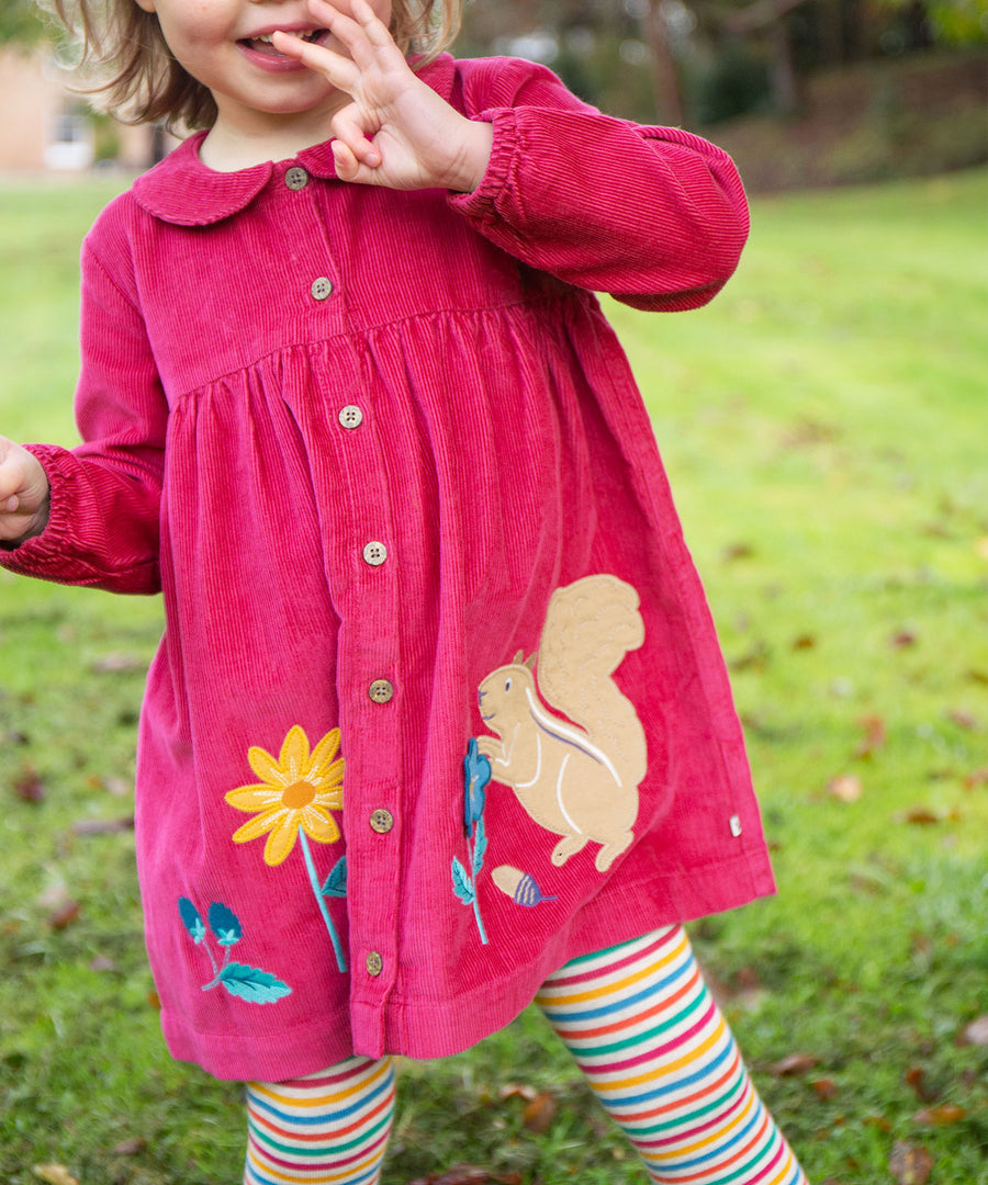 A child outside, wearing the Frugi Coco Cord Dress - Lingonberry/Squirrel