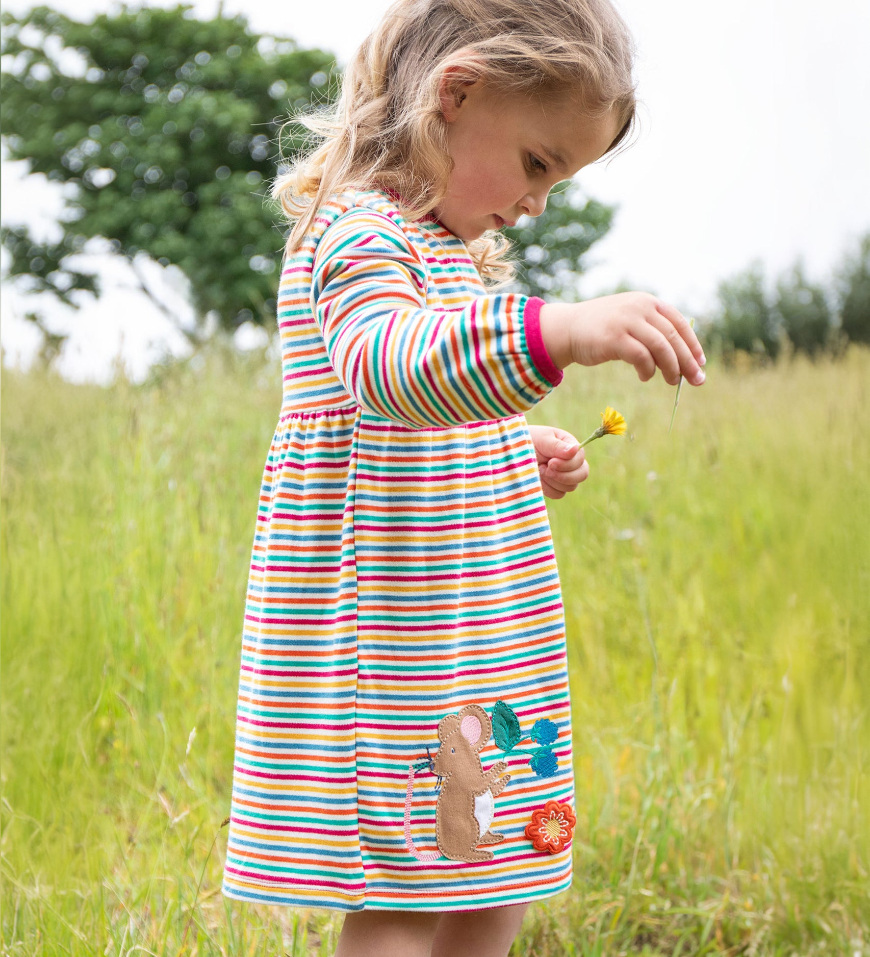 A child outside wearing the Frugi Dolcie Dress - Lingonberry Multi-Stripe