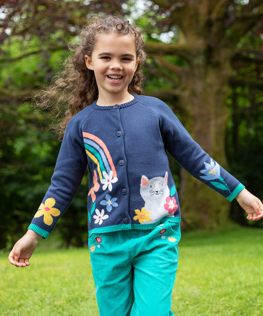 A child outside, wearing the Frugi Reva Knitted Cardigan - Navy Blue/Cat and green Frugi cord trousers