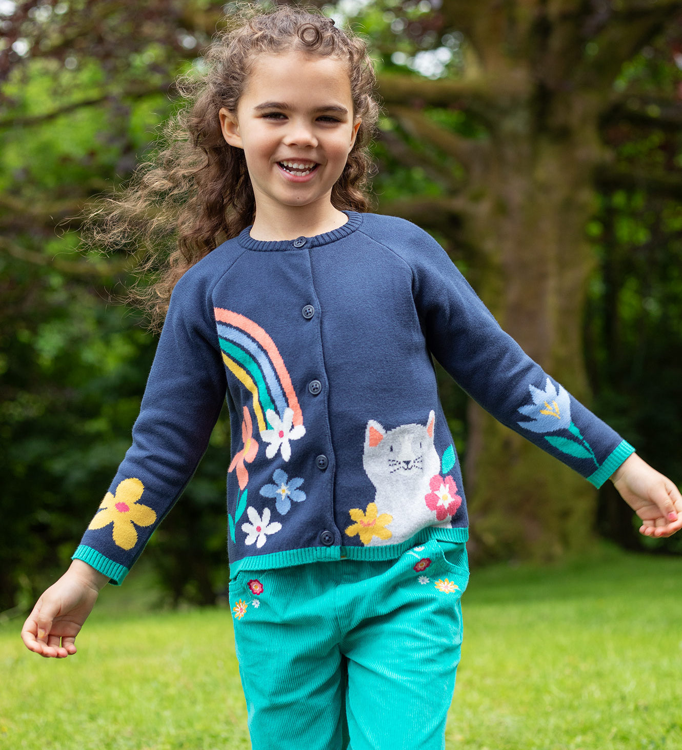 A child outside, wearing the Frugi Reva Knitted Cardigan - Navy Blue/Cat and green Frugi cord trousers