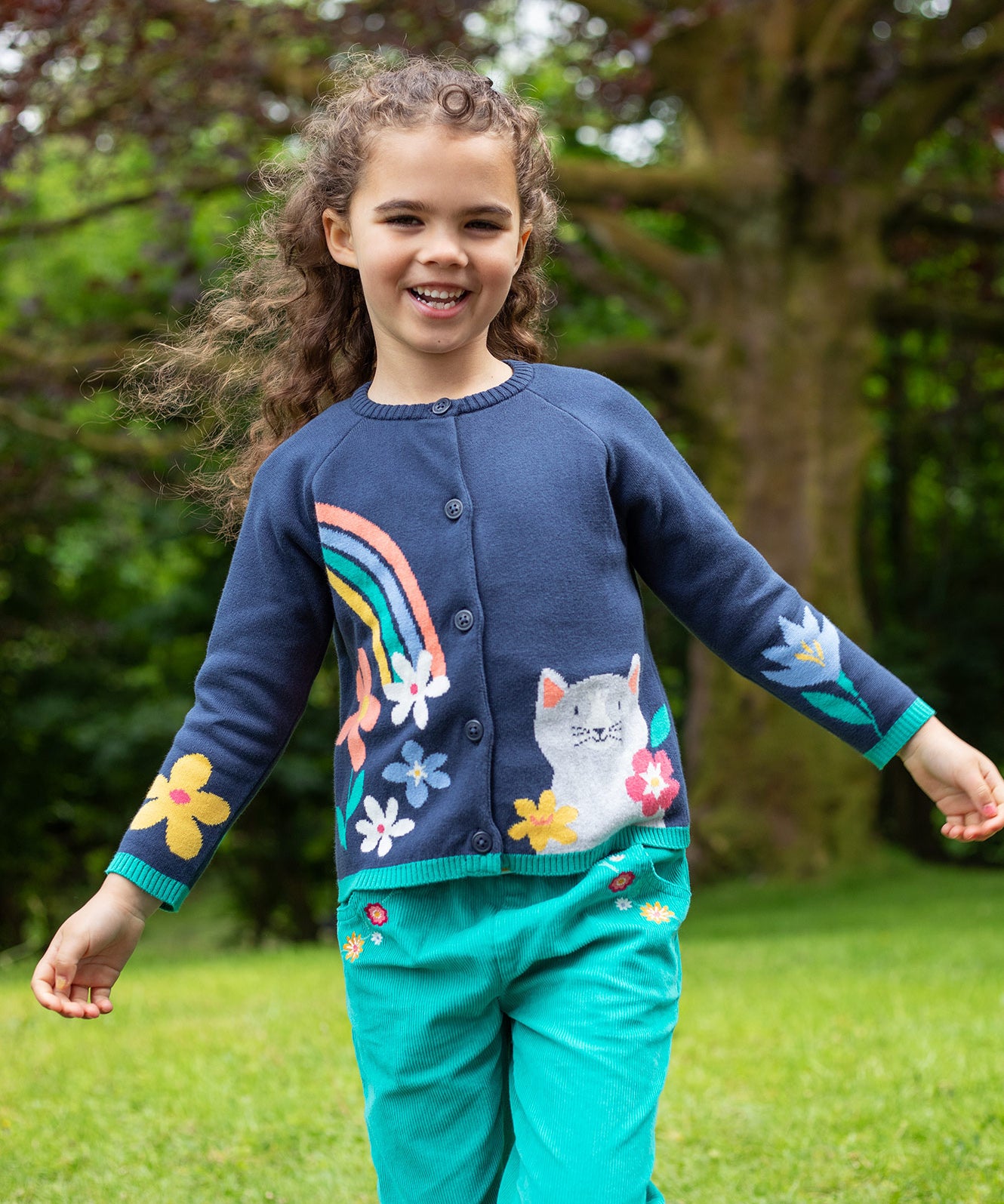 A child outside, wearing the Frugi Reva Knitted Cardigan - Navy Blue/Cat and green Frugi cord trousers