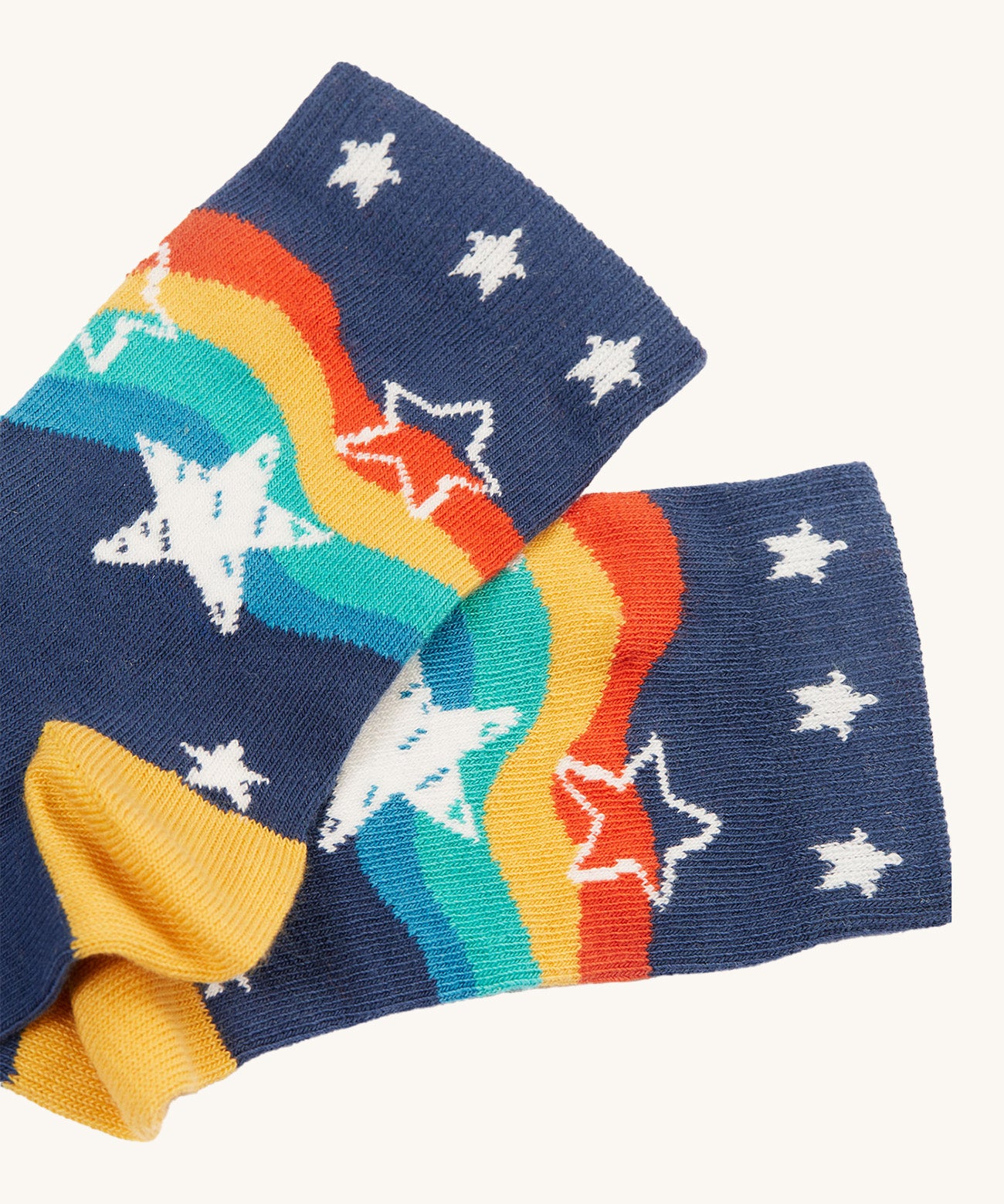 The navy blue pair of socks from the Frugi Rock My Socks - Stars 2 Pack. These navy socks have a rainbow wavy print on them with white stars, and white stars on the ankle cuffs